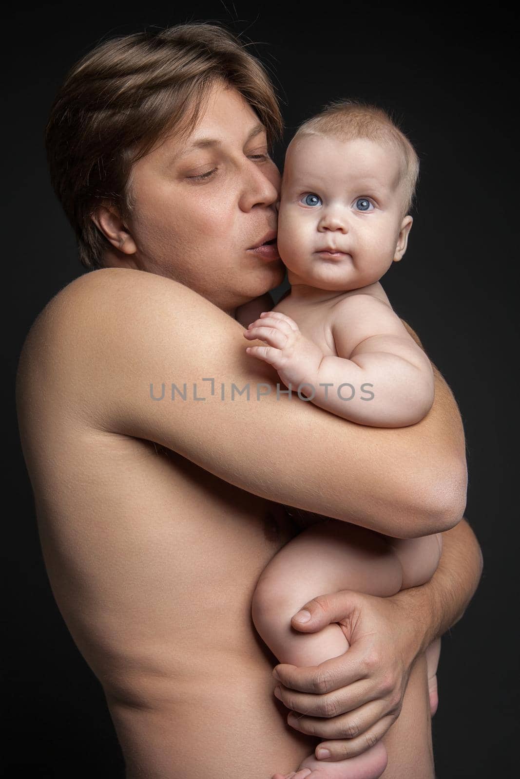 Happy father hugging and kissing his newborn baby.Isolated over black background.
