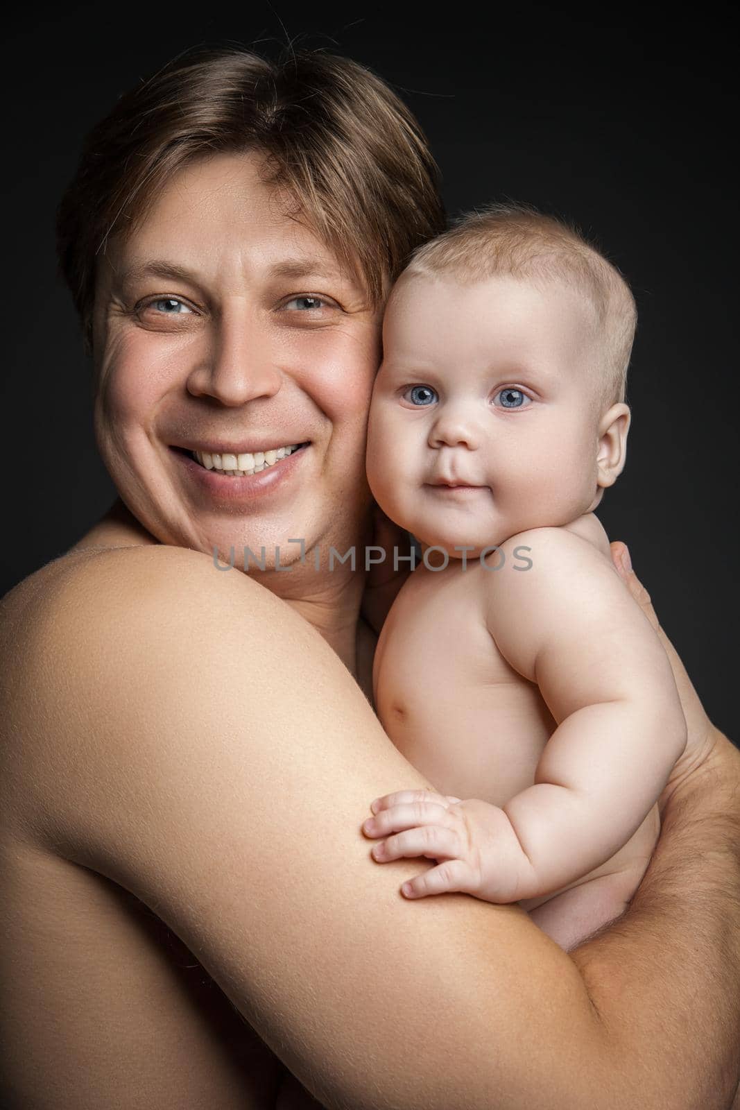 Father holding toddler son both looking at the camera. Both are smiling.