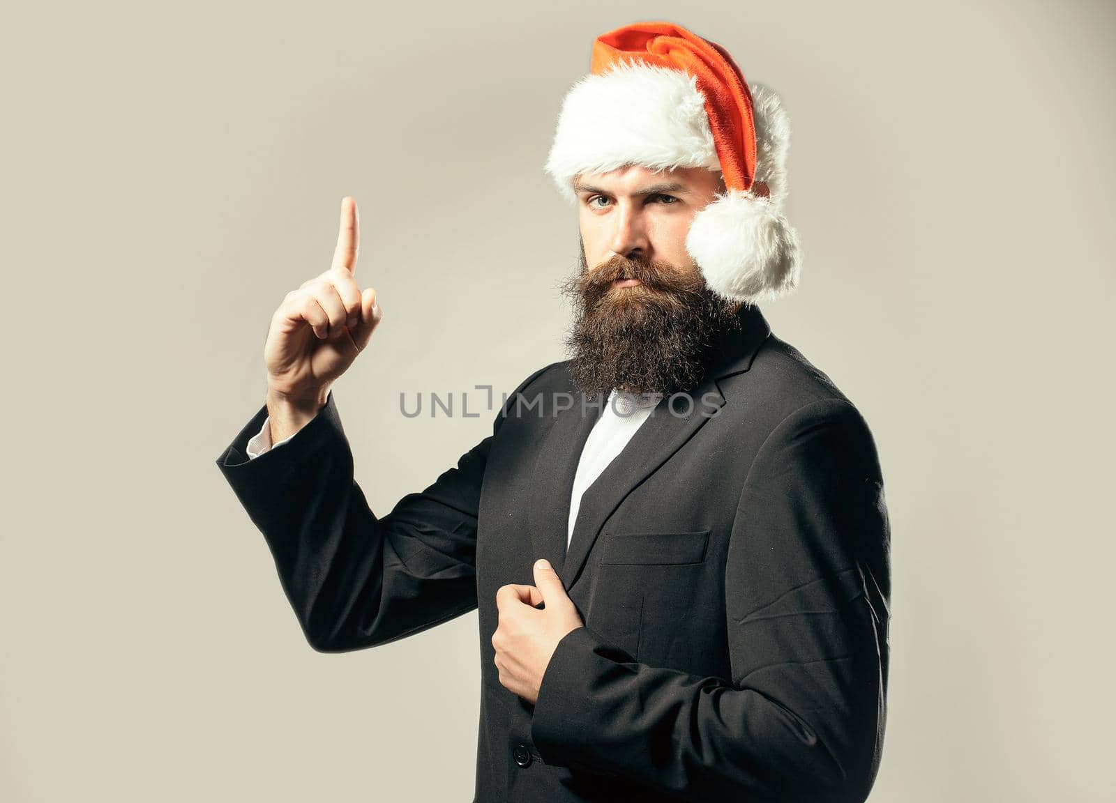Handsome serious man with beard and moustache in santa hat with raised finger on grey isolated background.