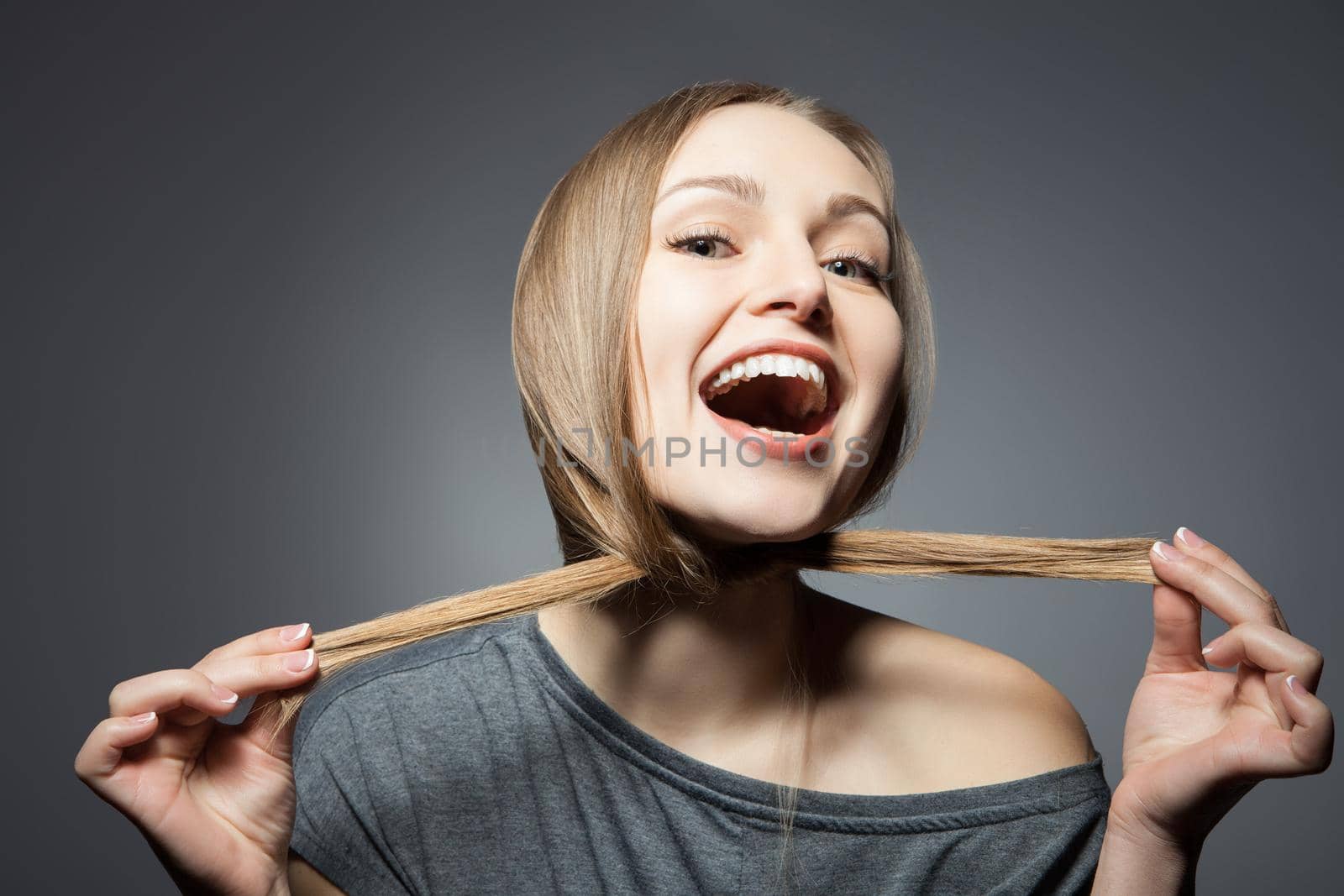 Smiling woman with mouth opened holding hair around face. Horizontal studio shot