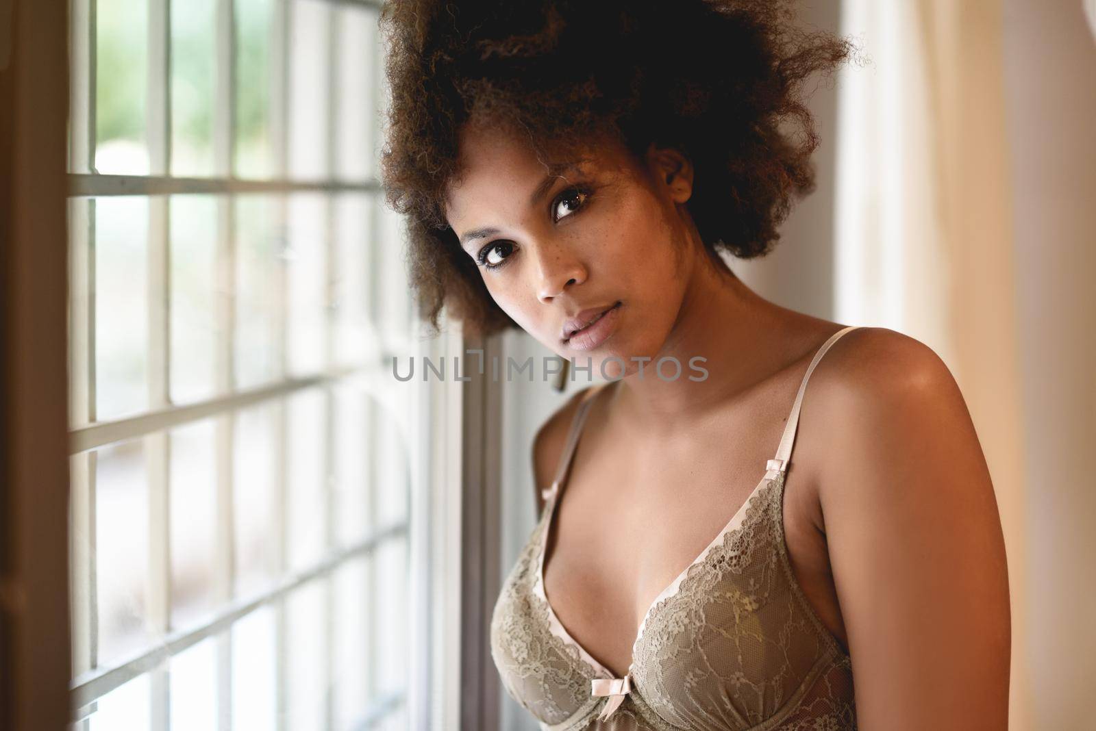 Young black woman with afro hairstyle in lingerie near a window. Mixed girl wearing underwear in her room.