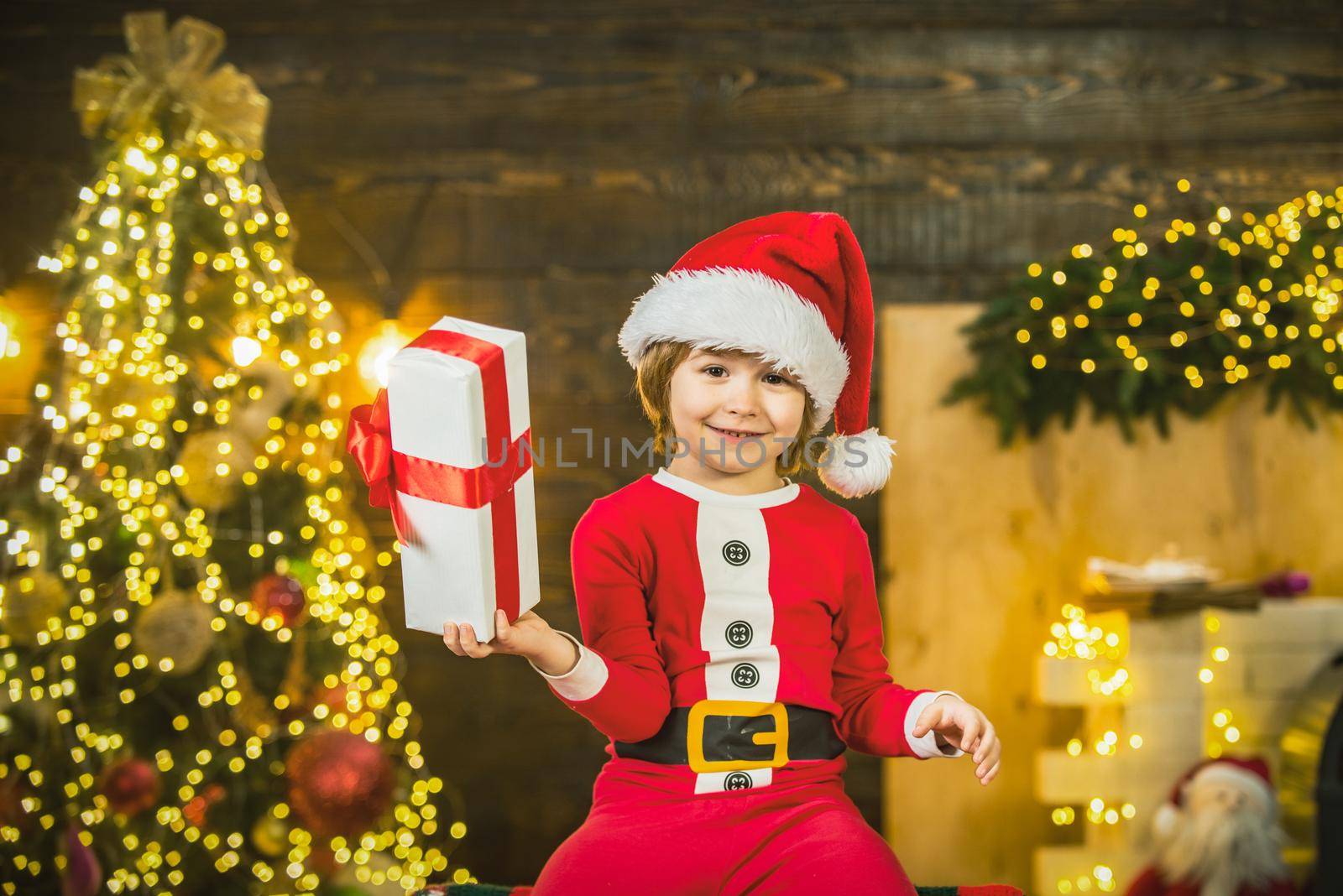 Happy cute child in Santa hat with present have a Christmas. Christmas kid boy gifting gift. by Tverdokhlib
