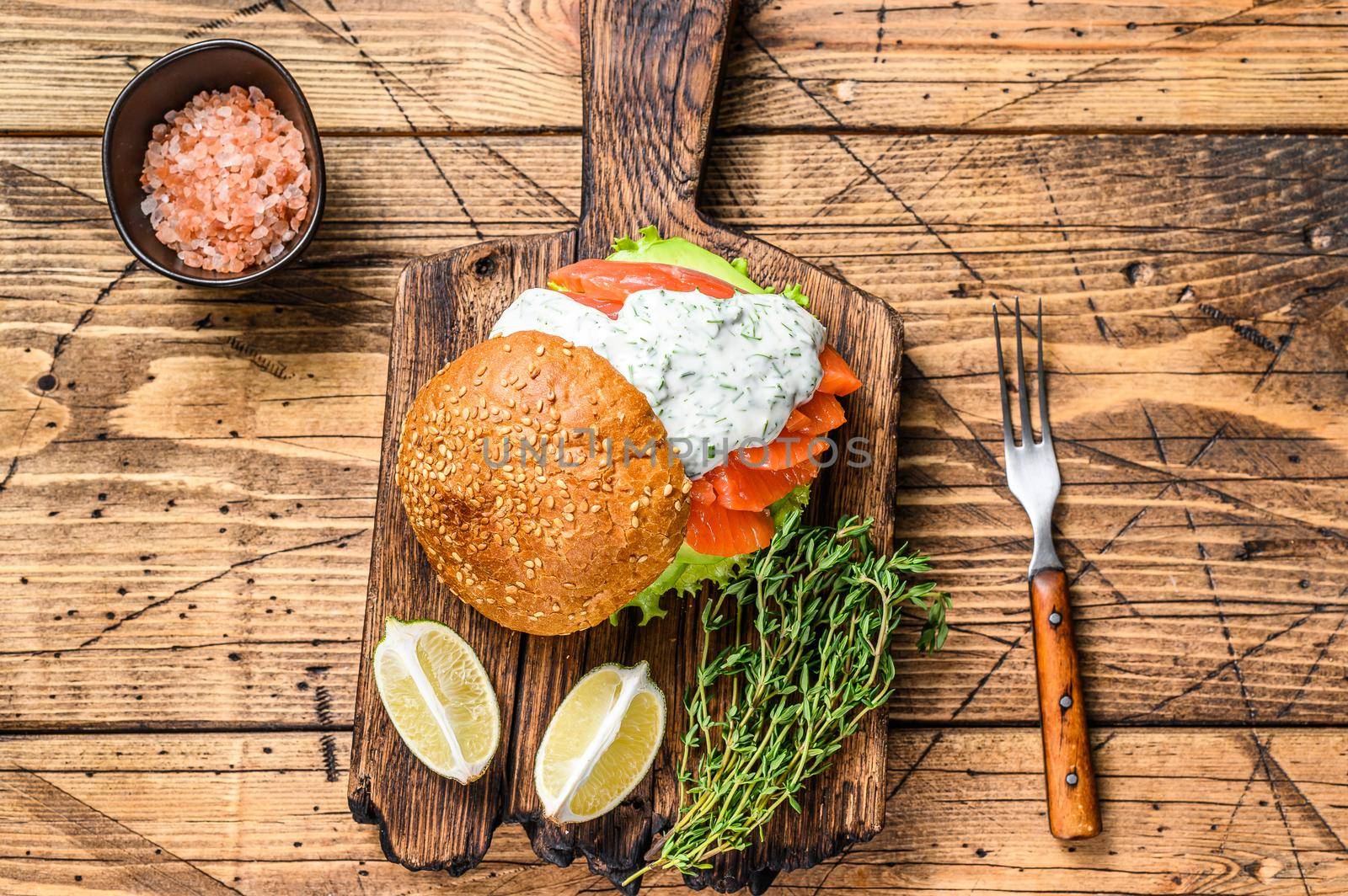 Sandwich with salted fish salmon, avocado, burger bun, mustard sauce and Iceberg salad. wooden background. top view.