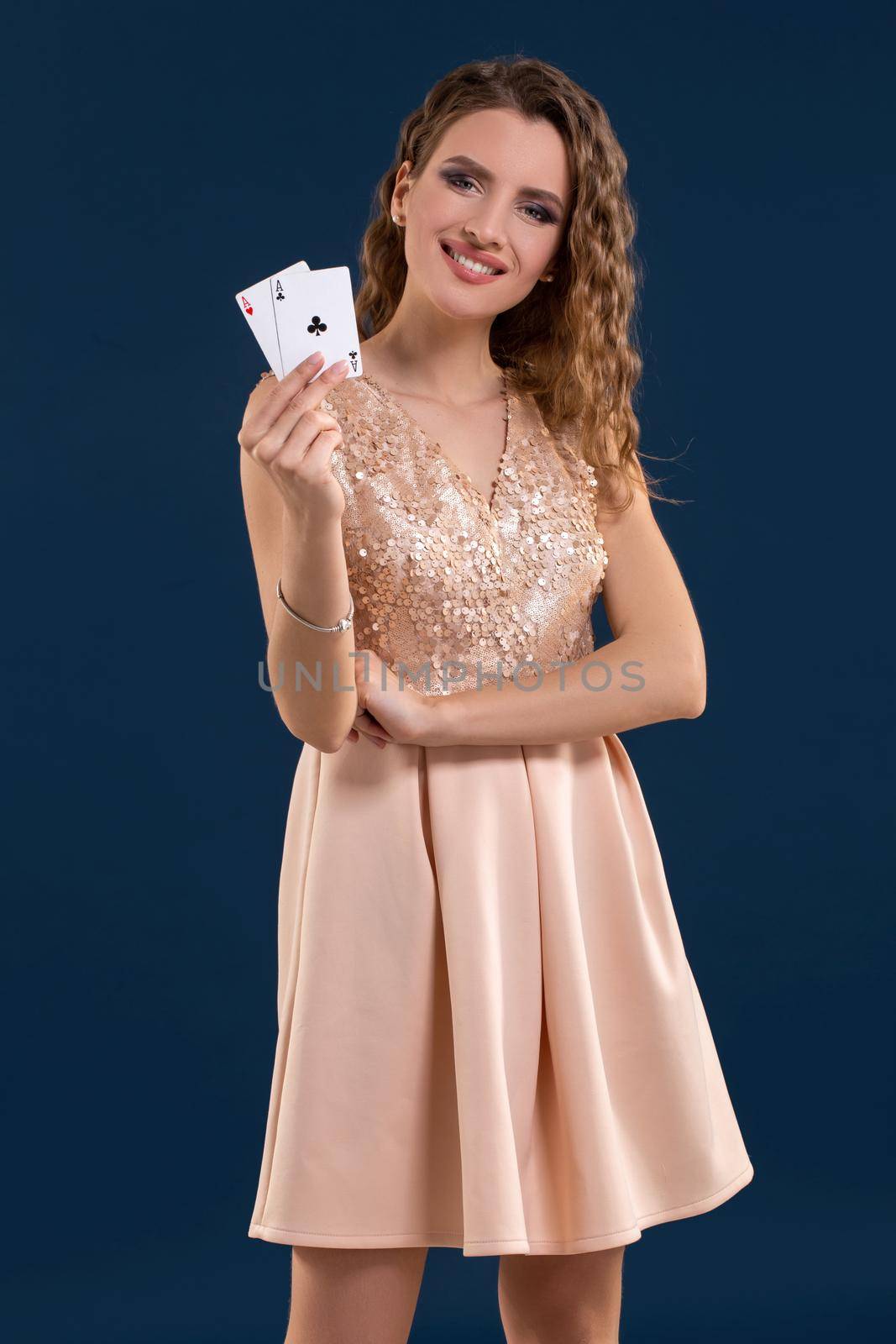 Young beautiful woman playing in casino. Woman in light dress holding the winning combination of poker cards on dark blue background. Two aces