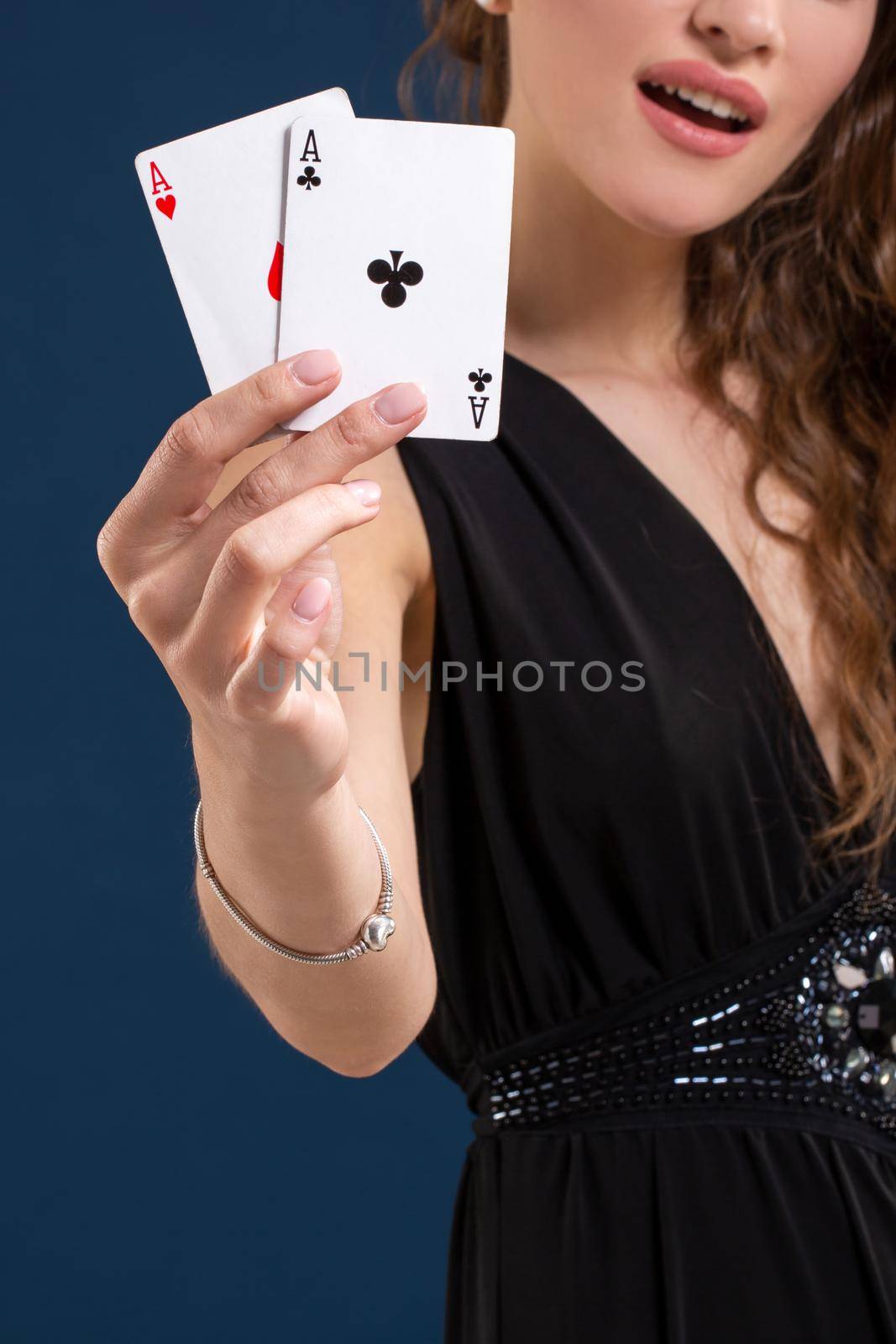 Beautiful woman in black dress holding two aces as a sign for poker game on dark blue background, gambling and casino. Close-up