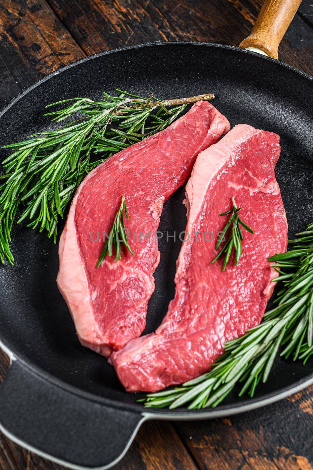 Raw beef meat rump steak in a pan. Dark wooden background. Top view.