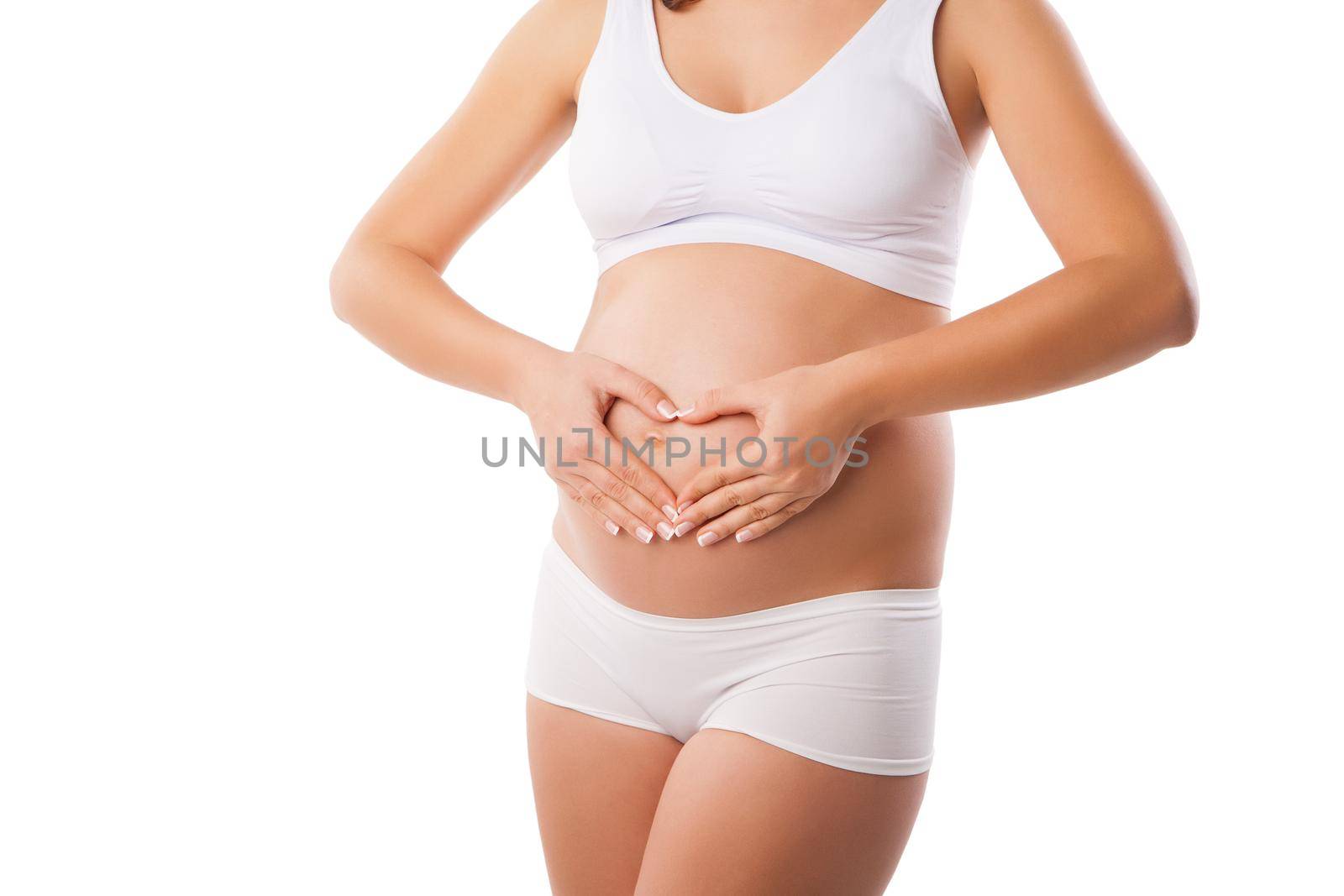 Pregnant woman forming heart out of her hands on her baby bump on white background.