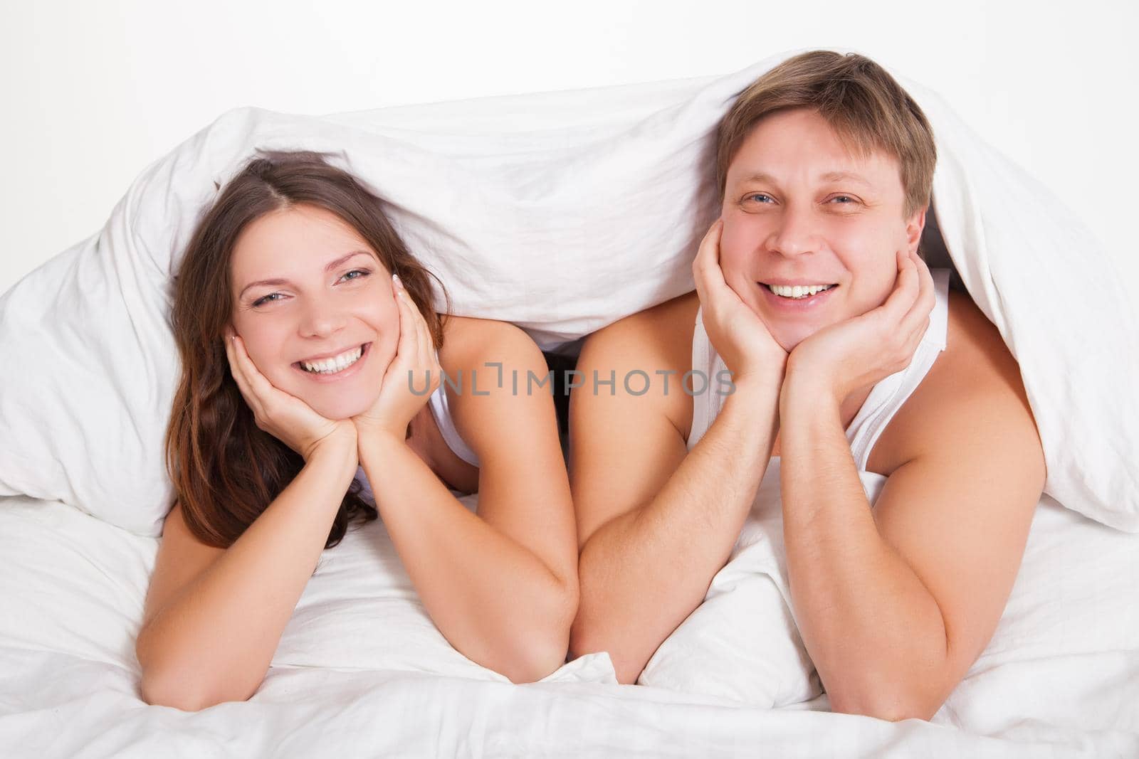 Beautiful young couple relaxing in bed at home over white