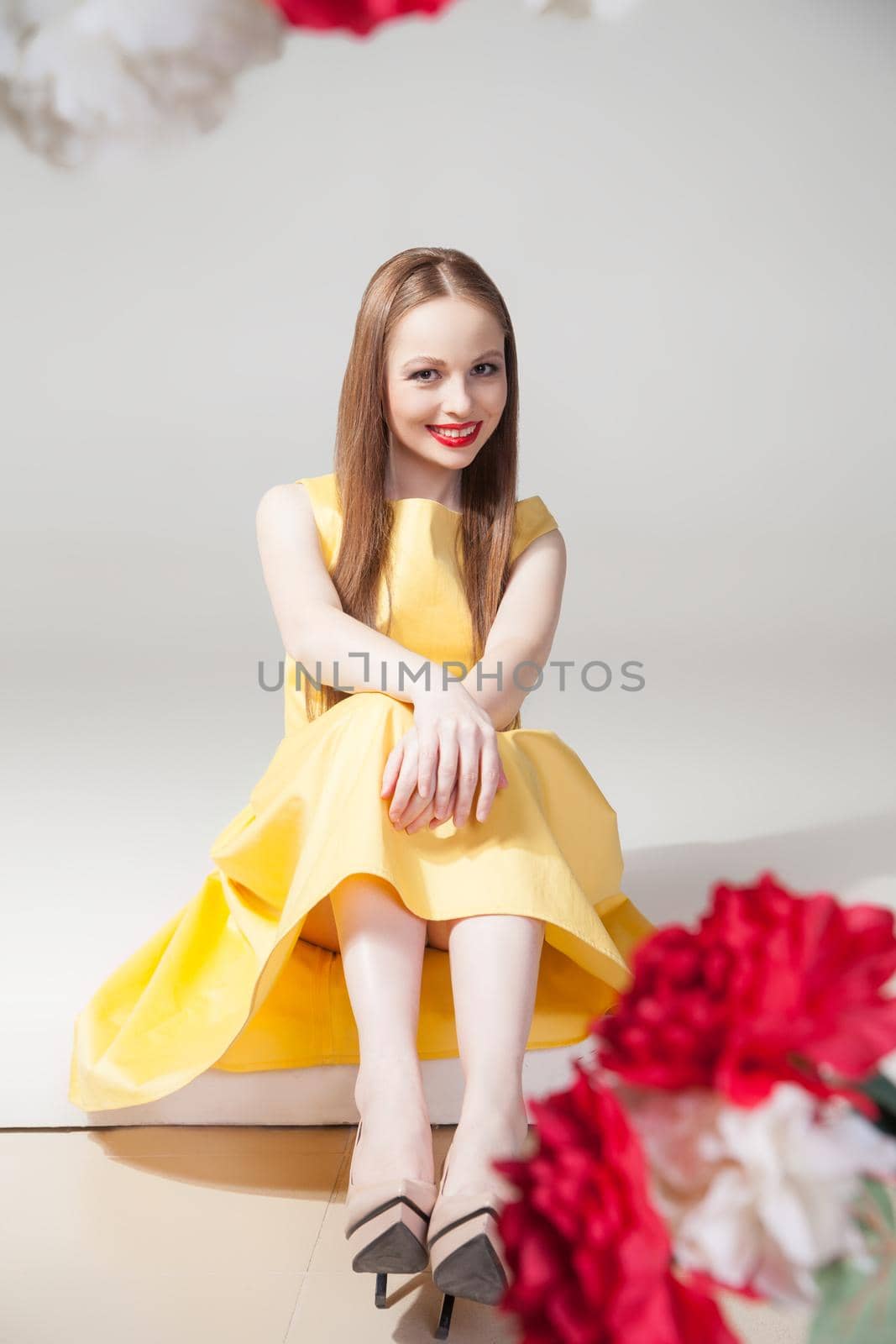 Portrait of beautiful smiling model sitting on floor in yellow dress.Studio shot.