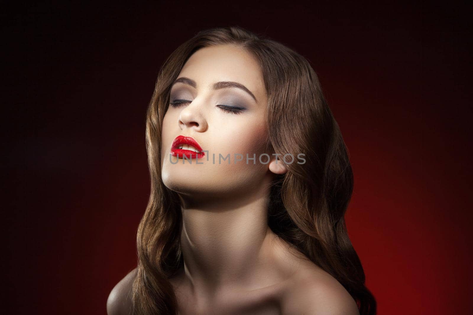 Portrait of young brunette with make-up and eyes closed against of red background