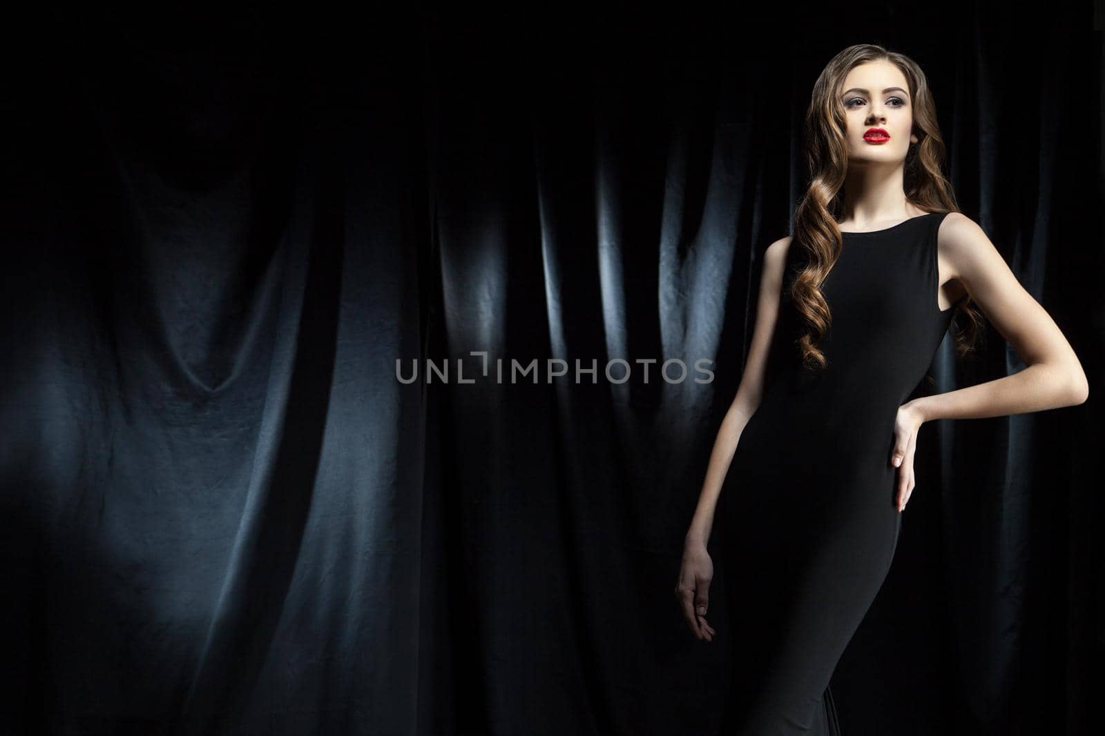 Portrait of elegant young woamn with long wavy hair in black dress looking away