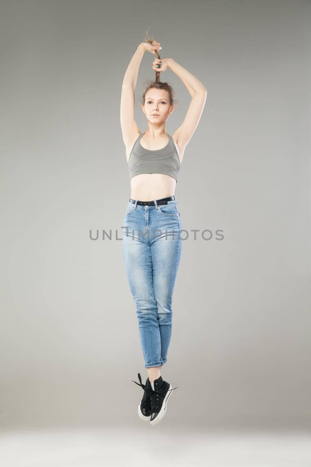 Portrait of blonde girl jumping and holding her hair in raised arms.Studio shot.Isolated