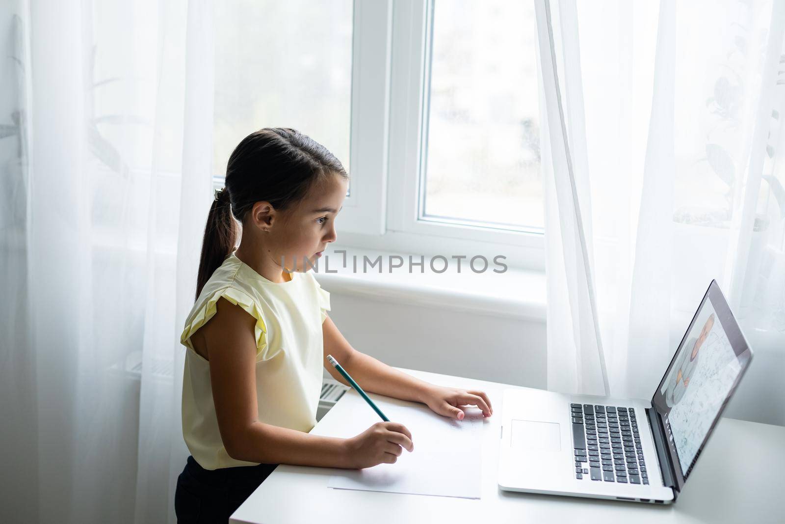 Litttle girl looking at laptop screen with expression of surprised and excitement. Smart, smilling little girl taking notes . Communication in business concept. by Andelov13
