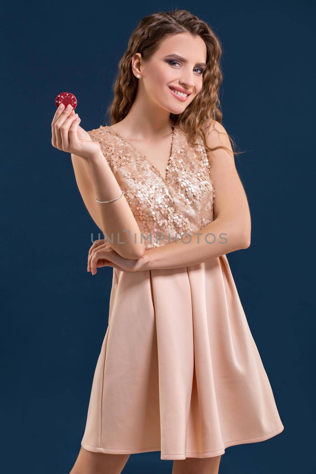 Beautiful young woman in dress with casino chips in the hands on dark blue background. Casino. Emotions. Gambling