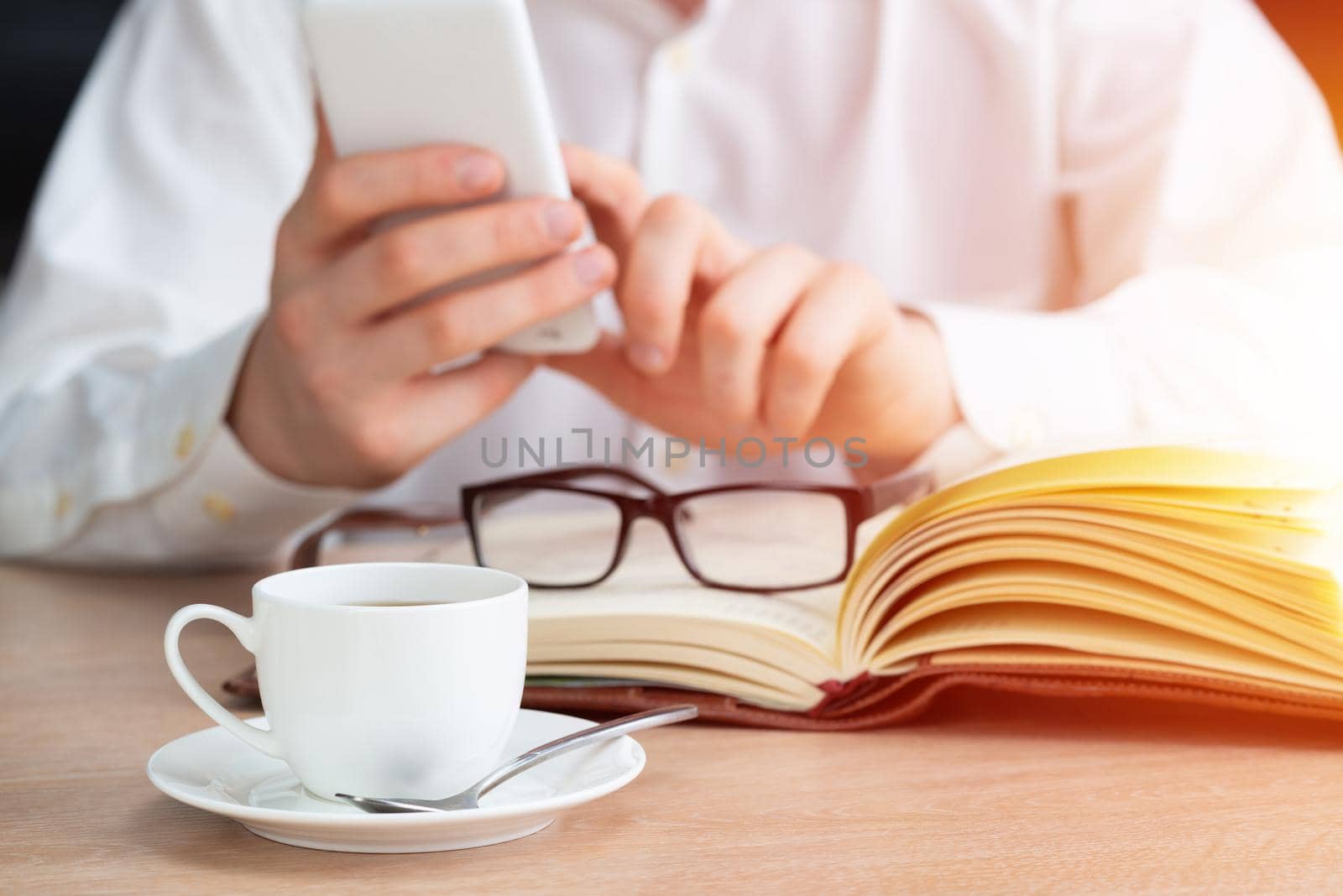 Man in white shirt using smartphone as sit at desk with cup of coffee. Business application and mobile technology. Internet internet browsing and communication. Coffee break at workplace in office