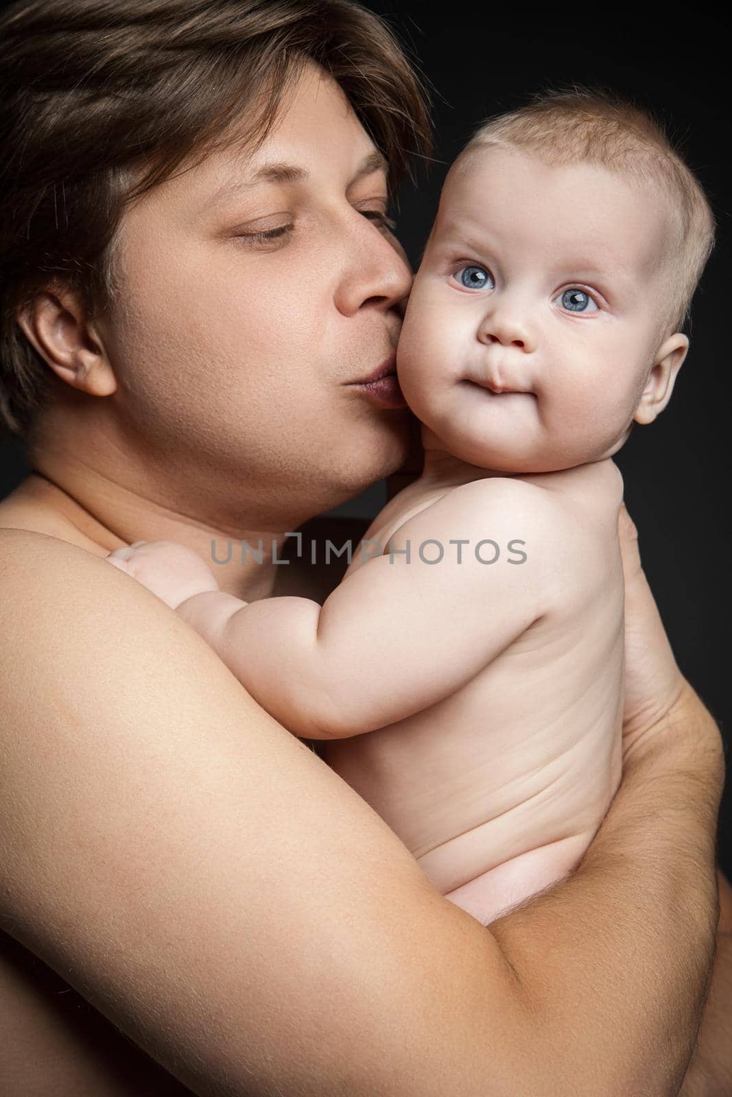 Happy father hugging and kissing his newborn baby.Isolated over black background. Close up.