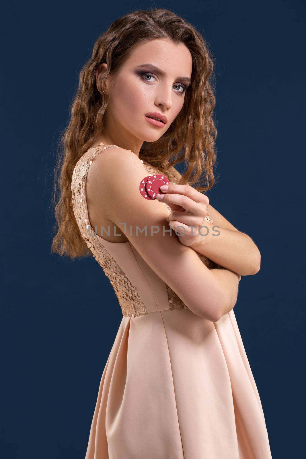 Beautiful young woman in dress with casino chips in the hands on dark blue background. Casino. Emotions. Gambling