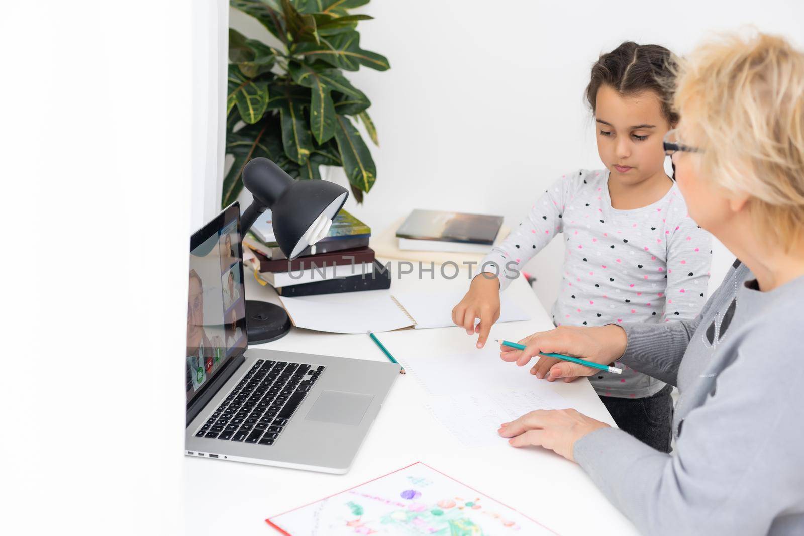 Cute and happy little girl child using laptop computer with her grandma, studying through online e-learning system.