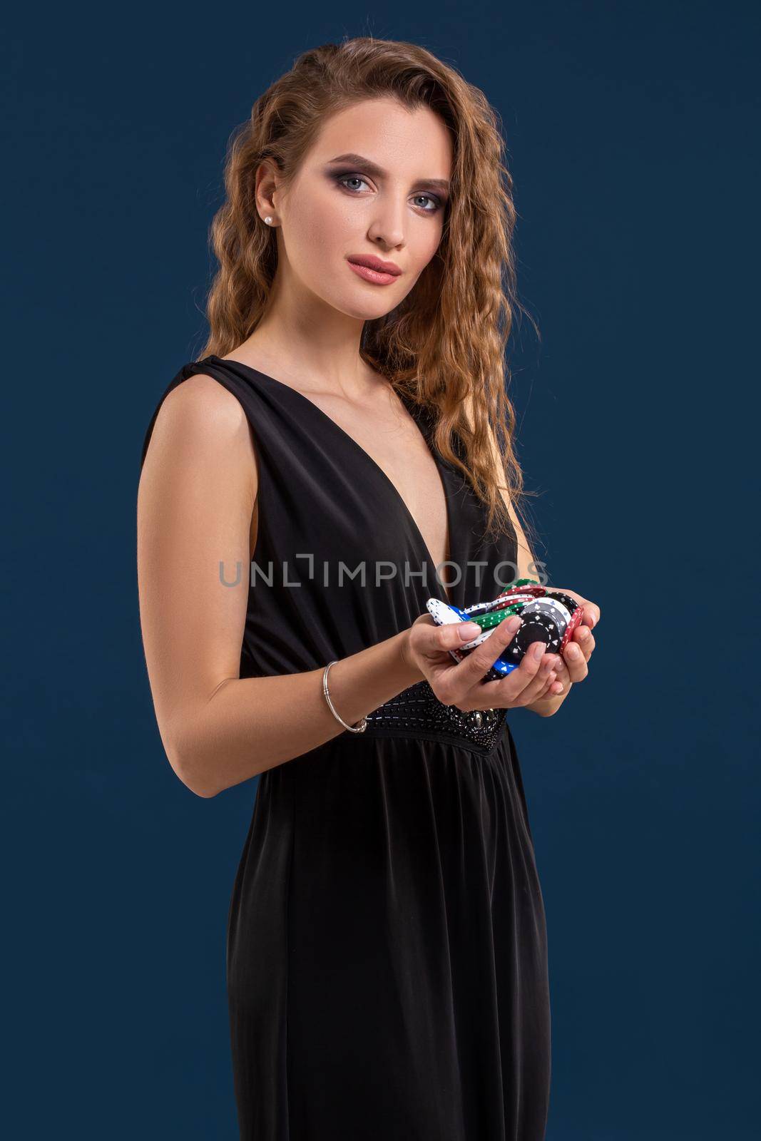 Elegant female casino player holding a handful of chips on dark blue background. A woman in a black dress with poker chips in her hands