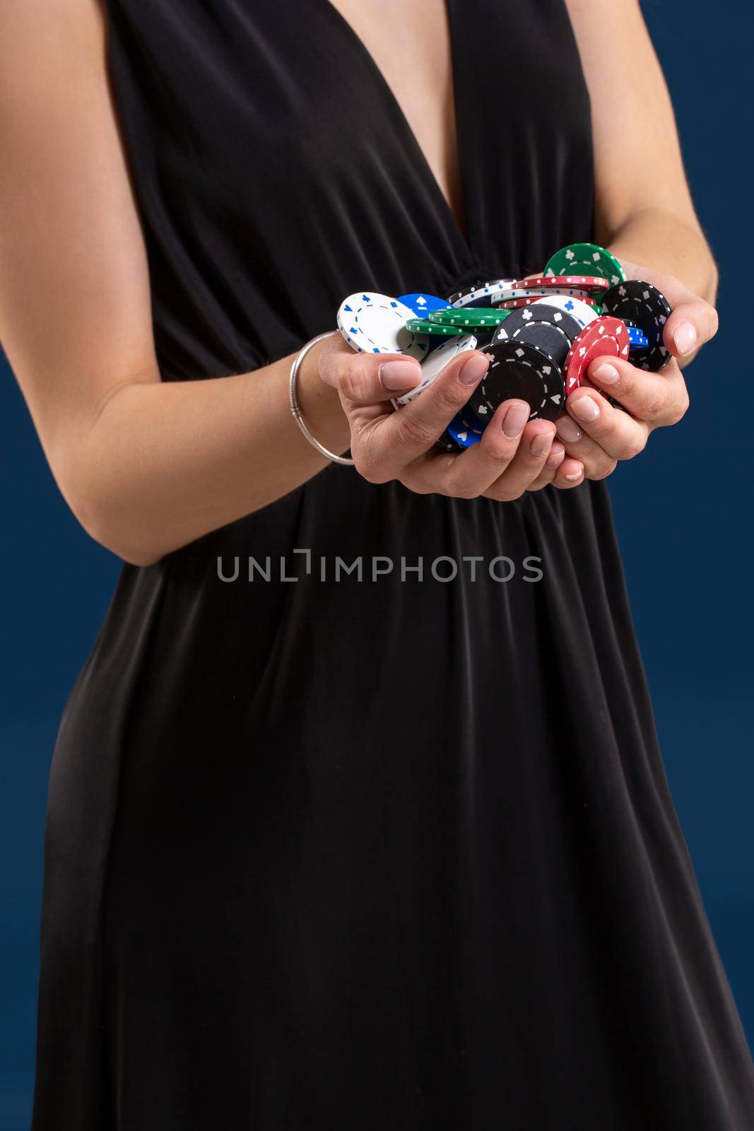 Elegant female casino player holding a handful of chips on dark blue background, hands close up. A woman in a black dress with poker chips in her hands
