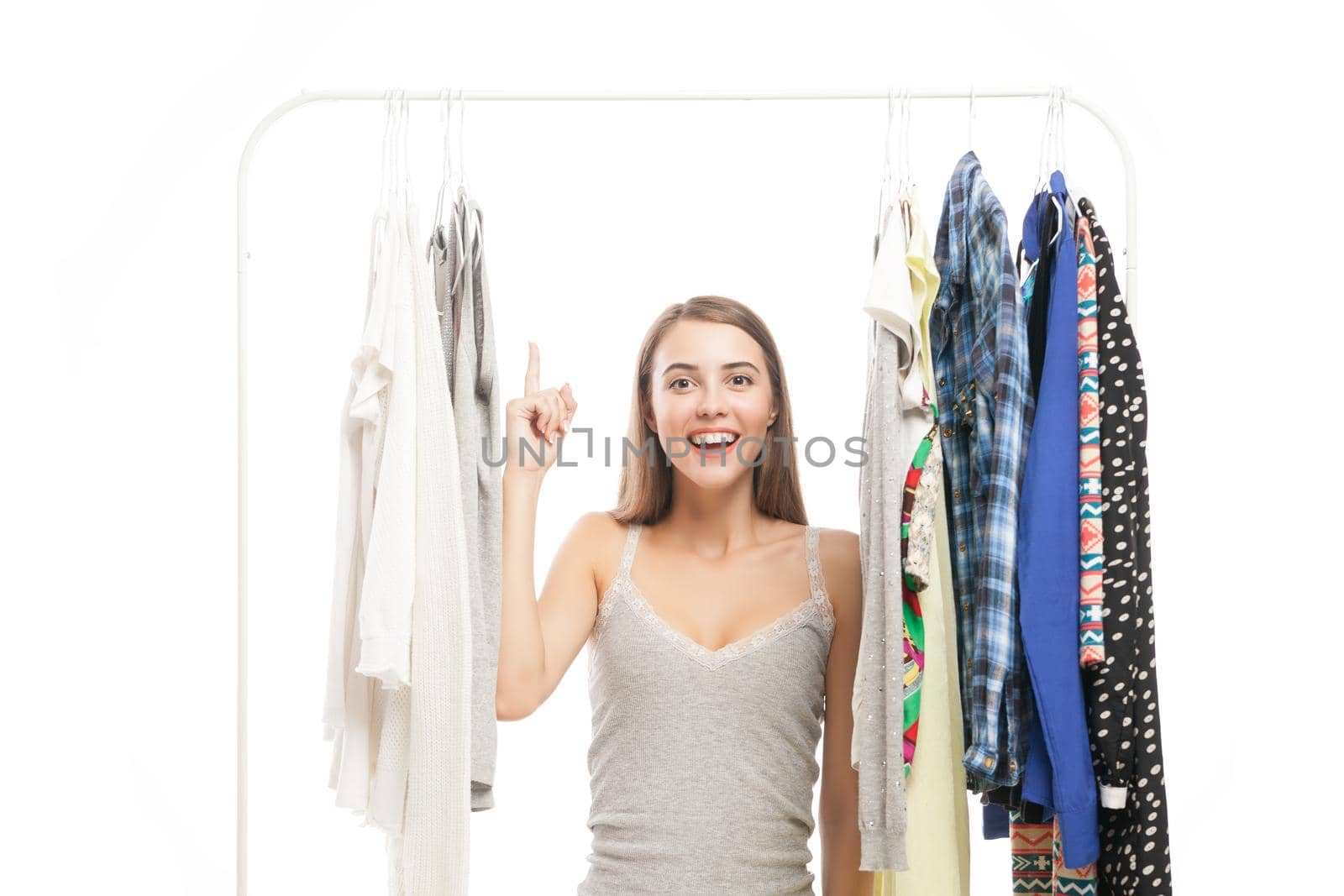 Portrait of smiling brunette with finger up looking at camera while standing between clothes