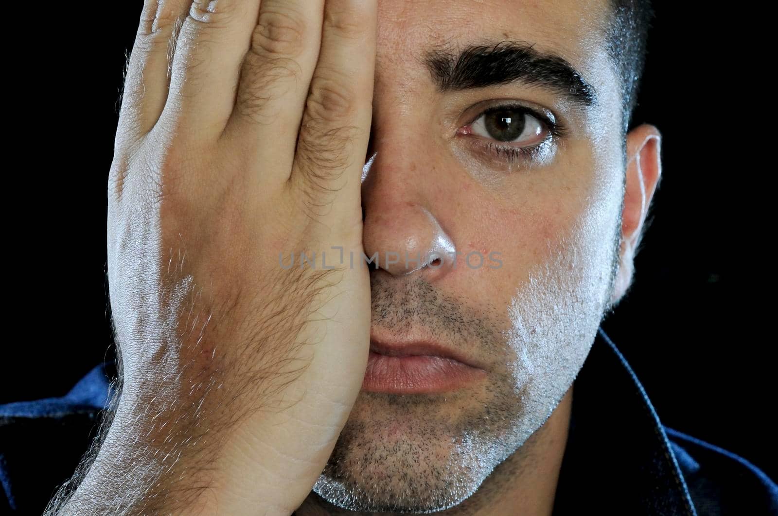 Study portrait of an attractive middle-aged man covering one eye with his hand.