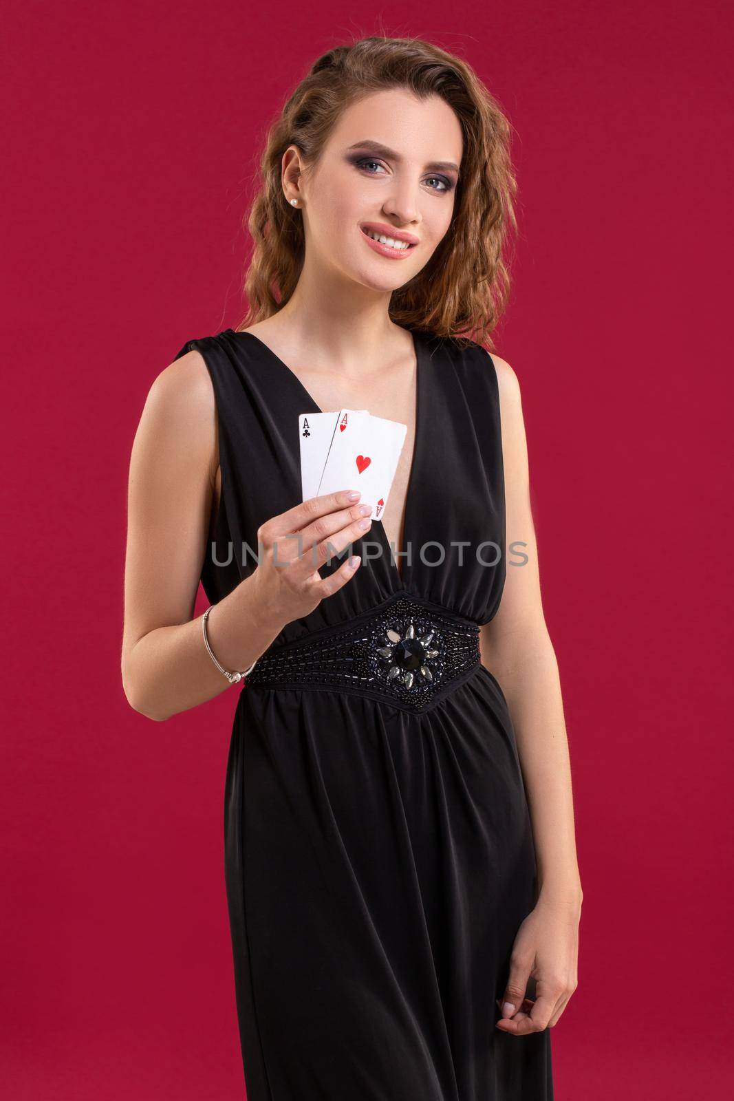 Beautiful young woman in black dress with a playing cards on red background. Casino. Poker