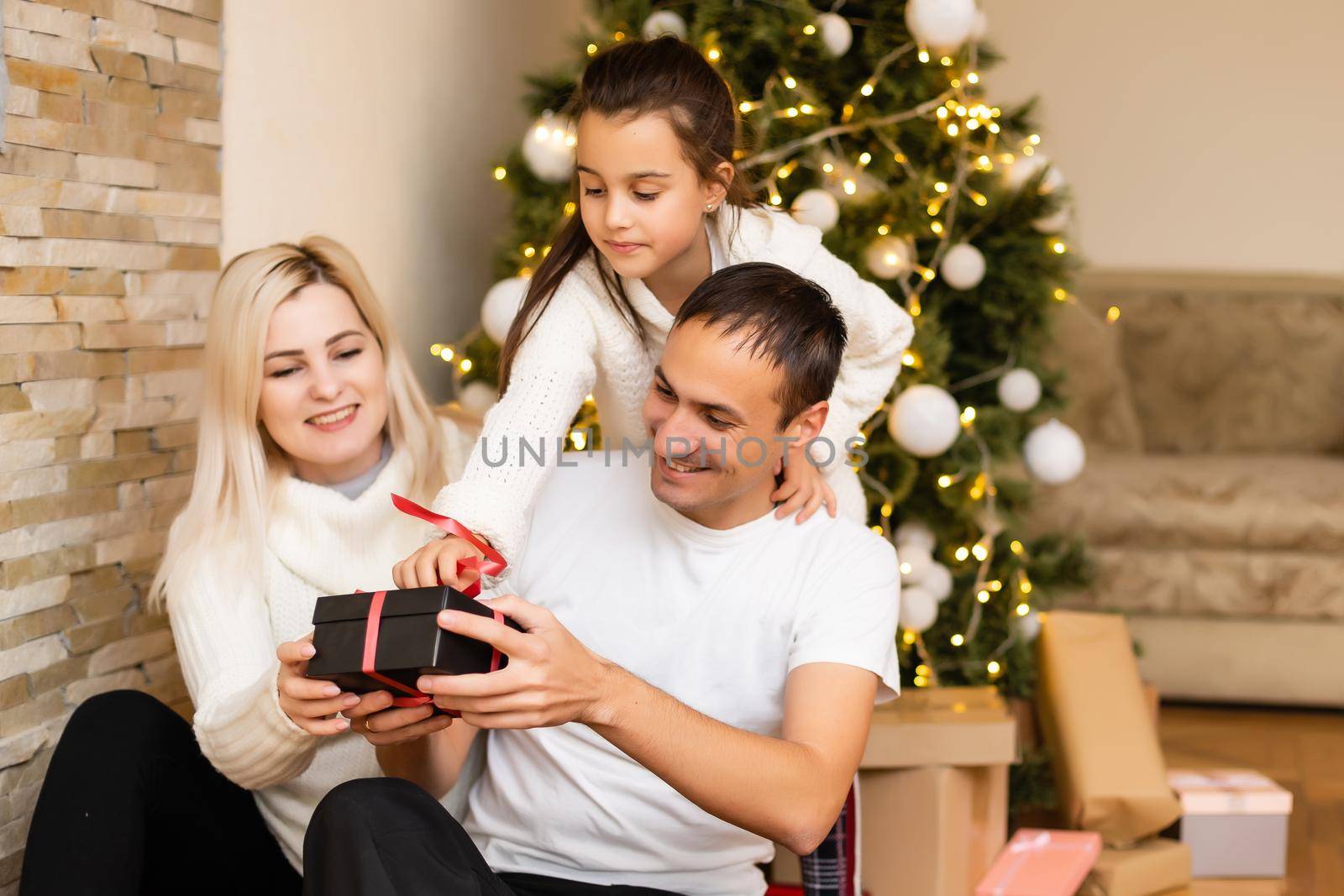 Family sitting on a floor. smiling mother, father and little girl near christmas tree.