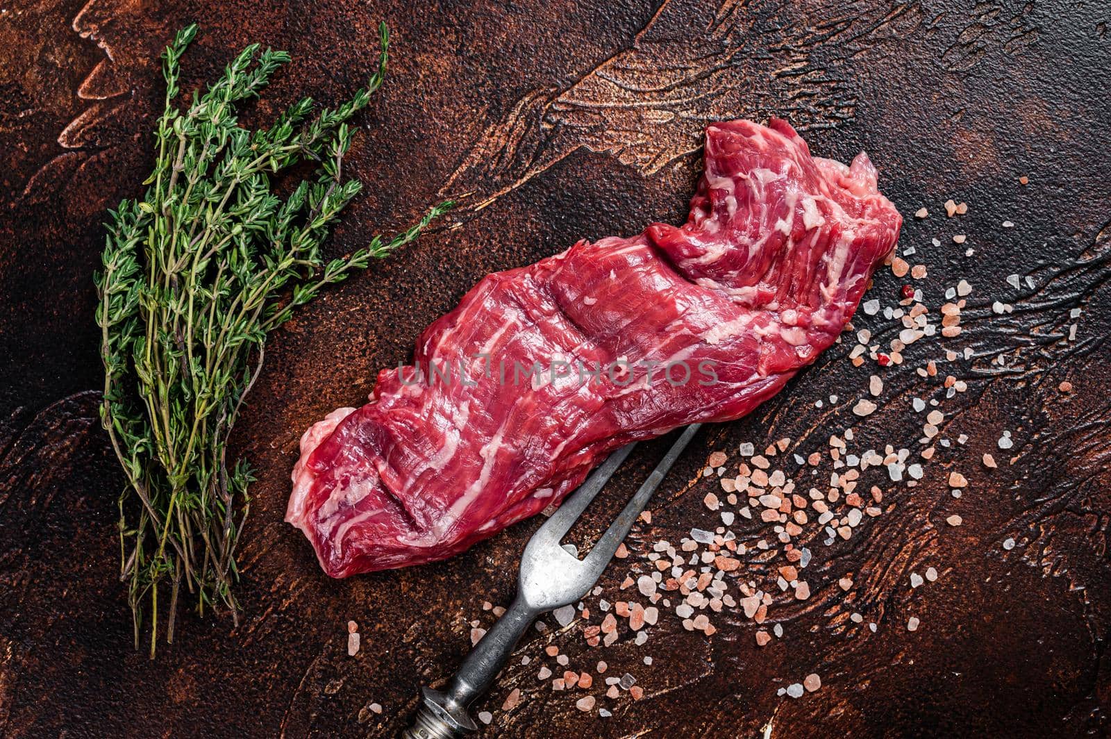Raw machete skirt beef steak on meat fork. Dark background. Top view by Composter