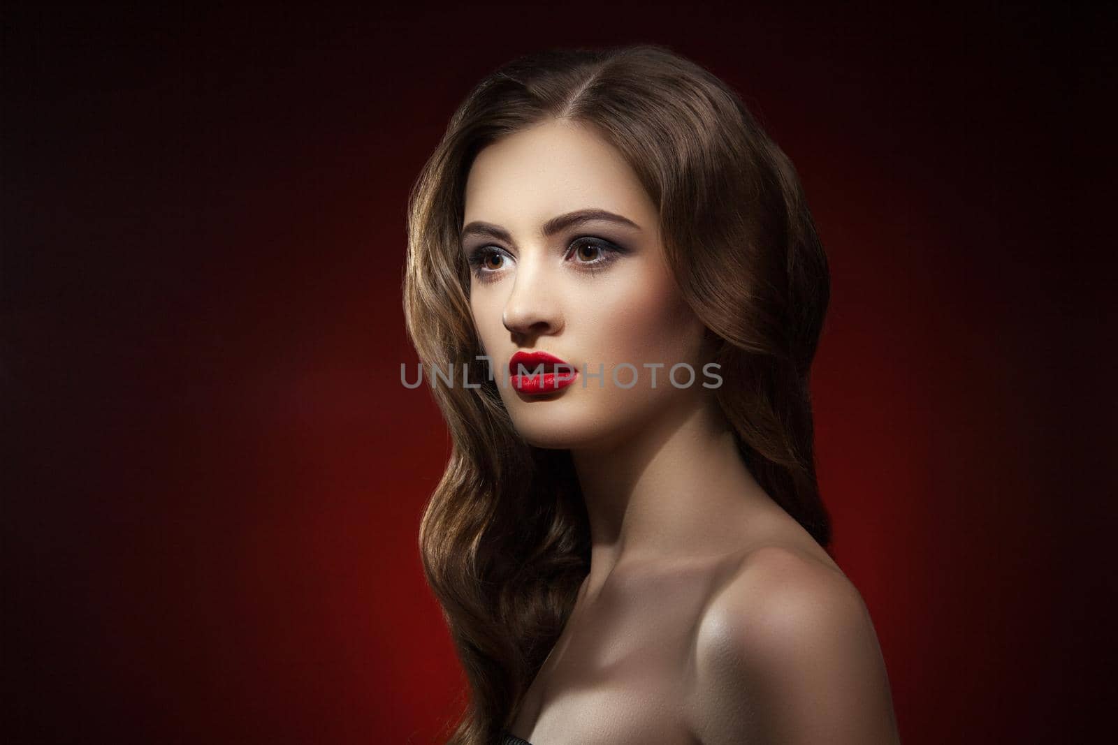 Close-up of beautiful young woman with bright red lips looking away against of red background