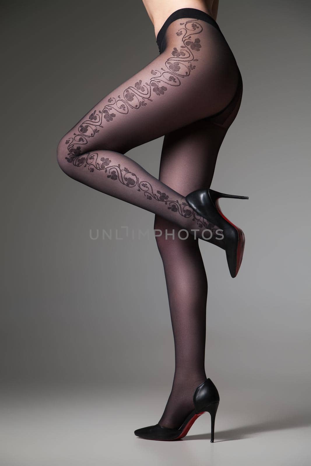 Vertical studio crop shot of female with on leg up posing in tights.