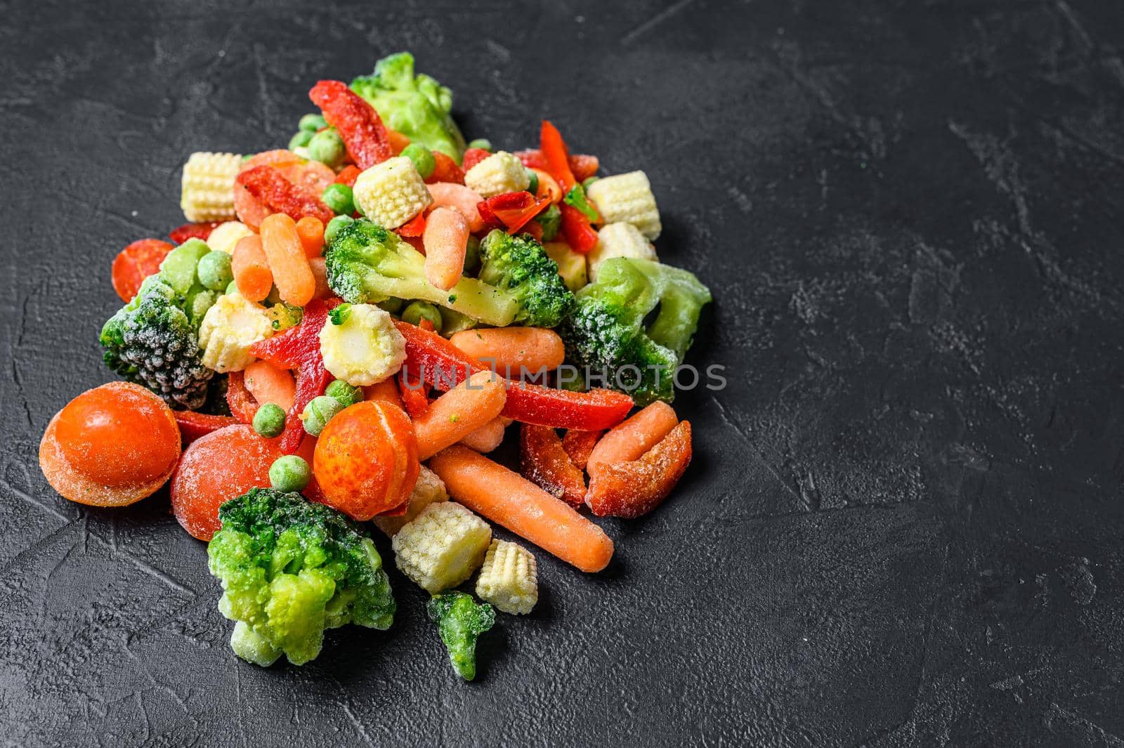 Frozen cold sliced Vegetables, broccoli, sweet peppers, tomatoes, carrots, peas and corn. Black background. top view. Copy space.