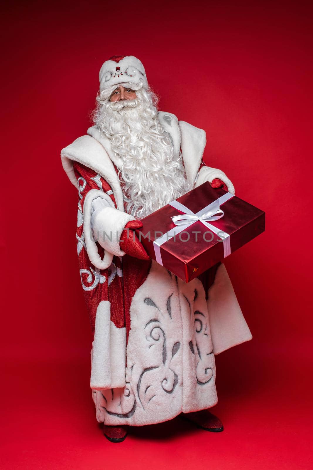 Full length Santa Claus with xmas gift on red studio background. High quality photo