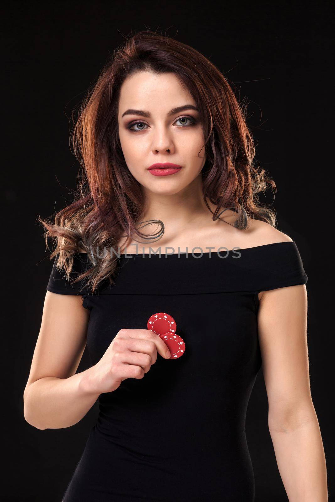 Smiling girl holding a gambling chips in her hands on black background. Sexy brunette in a dress. Poker.