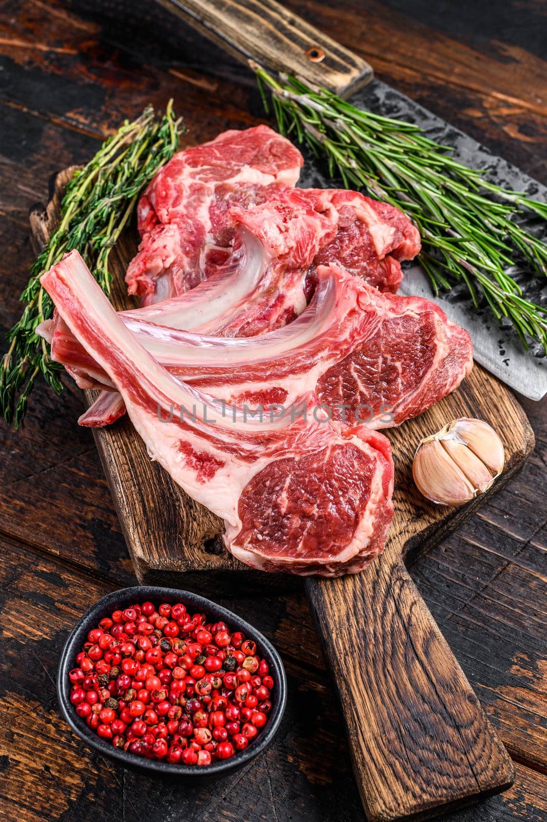 Lamb raw chops steaks on butcher cutting board. Dark wooden background. Top view.