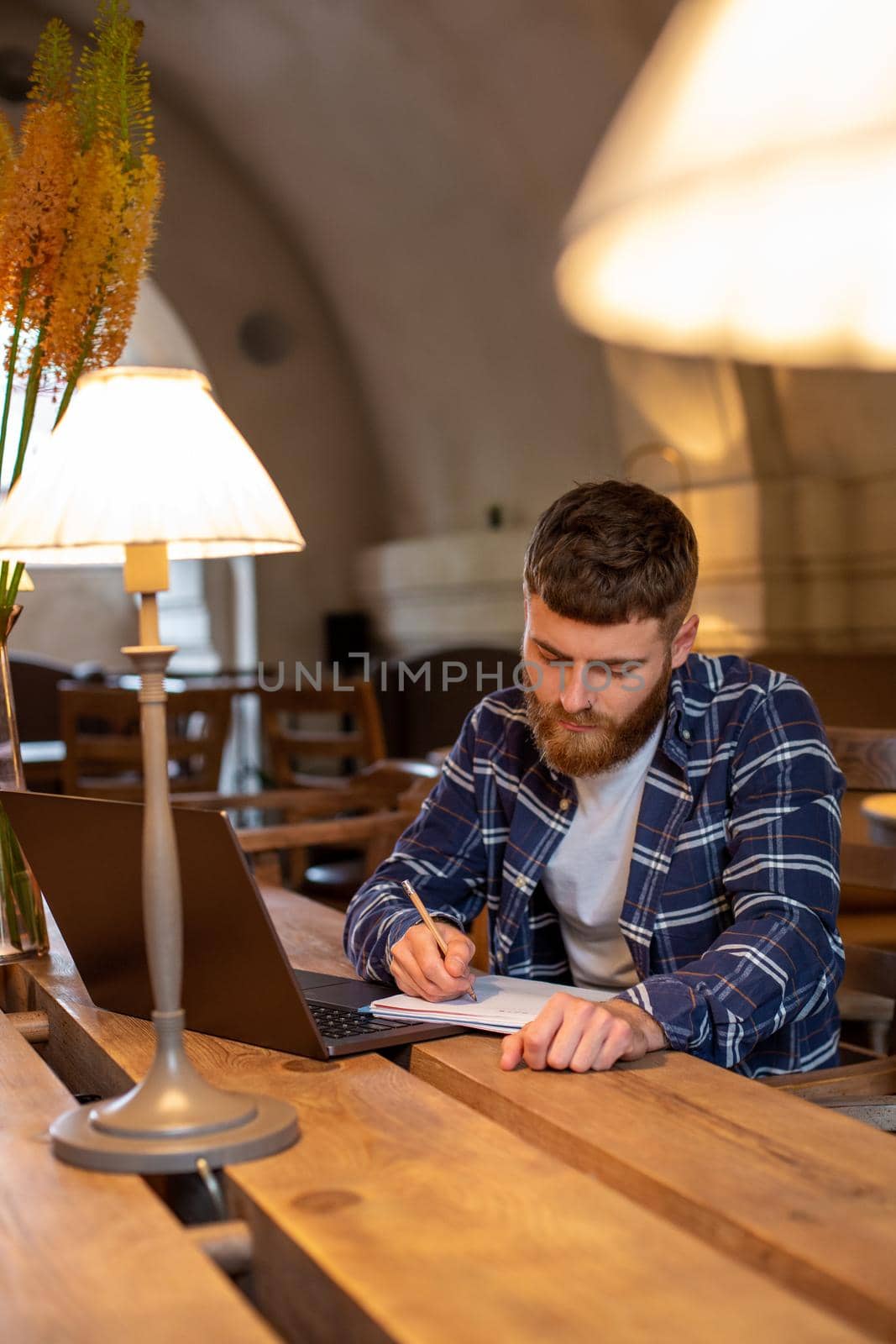 Casual business man or freelancer planning his work on notebook, working on laptop computer with smart phone, cup of coffee on table at coffee shop or home office, working from cafe concept