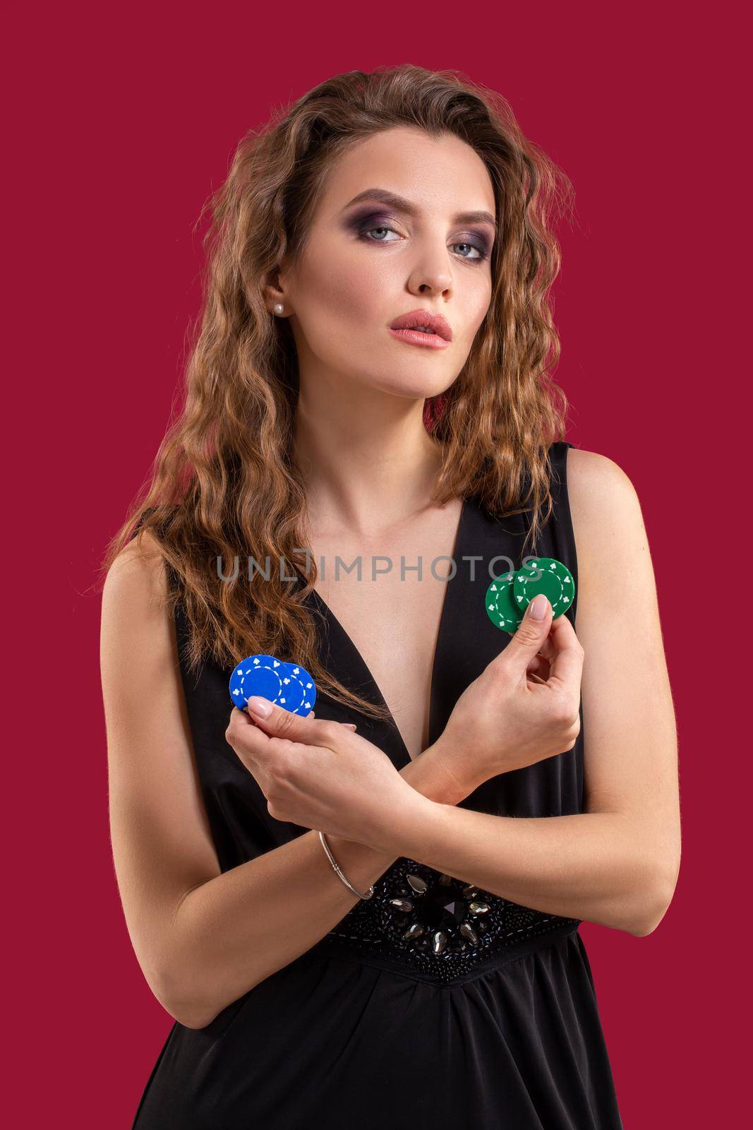 Pretty long hair woman in black dress holding chips for gambling on red background. Studio shot