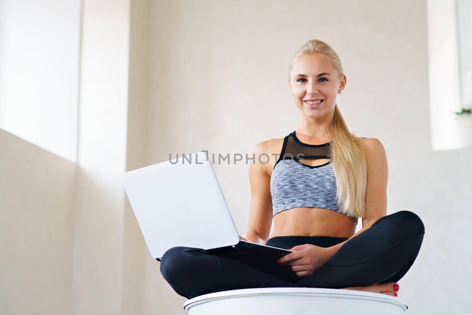 Sports business girl with laptop in lotus pose looks at camera and smiles