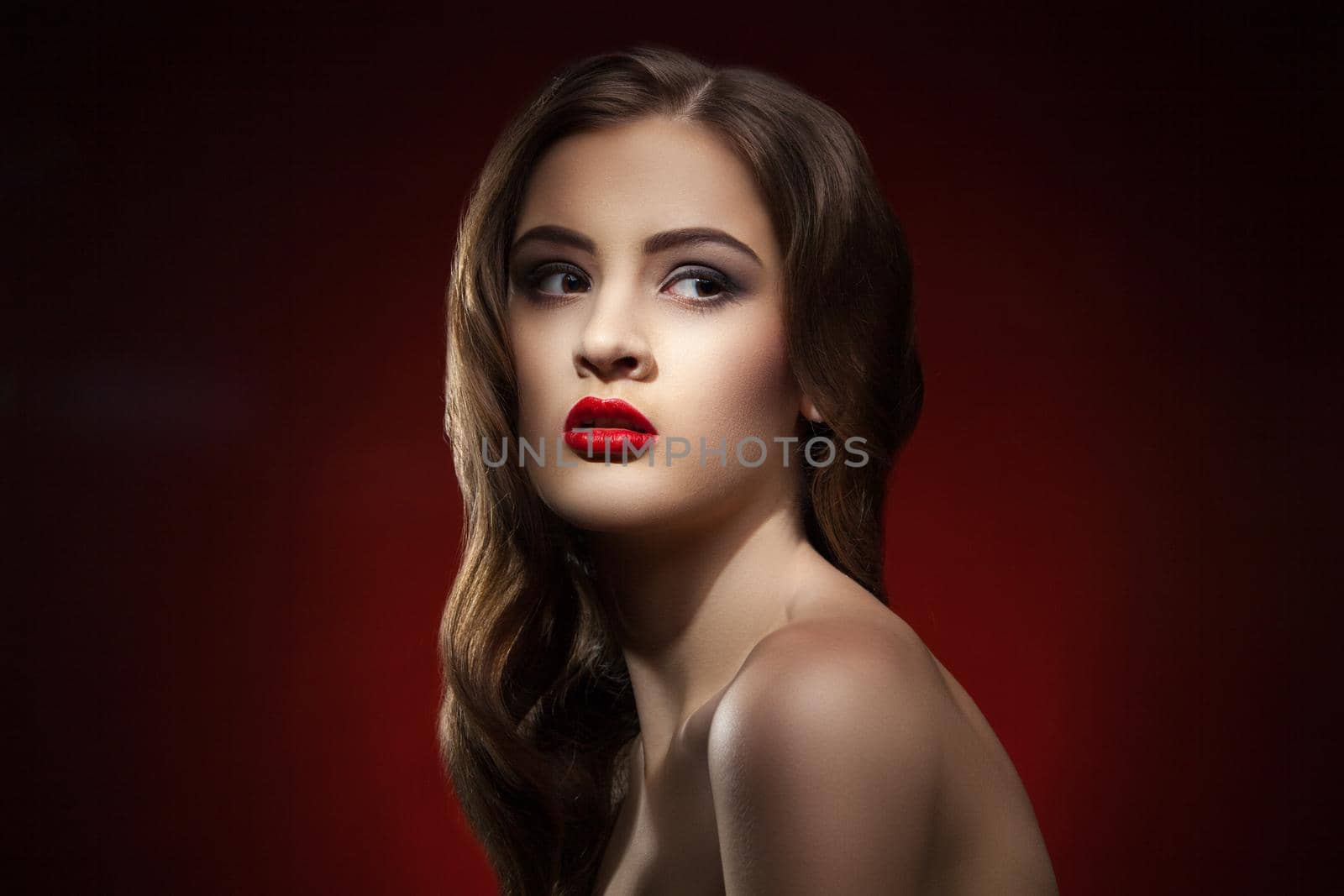 Close-up of beautiful young woman with bright red lips looking away against of red background