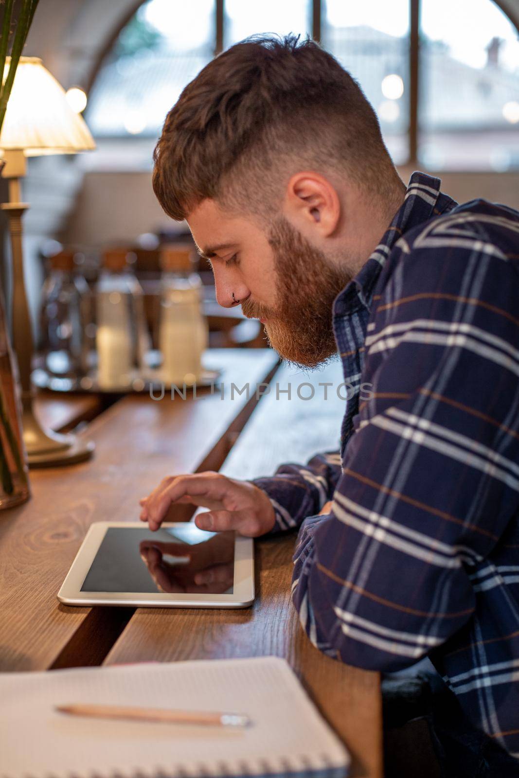 Freelancer dressed in casual outfit focus on reading news and looking on digital tablet while sitting in cozy urban cafe. Young man using modern technology for search job vacancy in internet