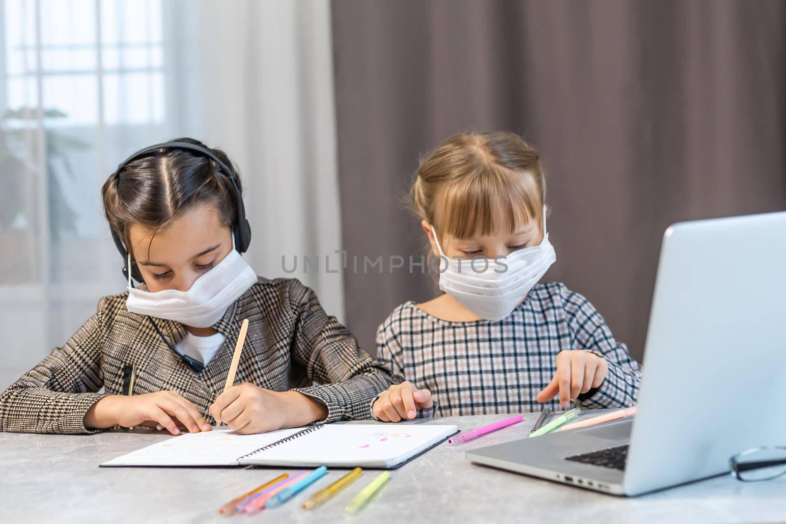 Distance Learning. School Girls At Laptop Wearing Mask Studying Online Sitting at the table at home by Andelov13