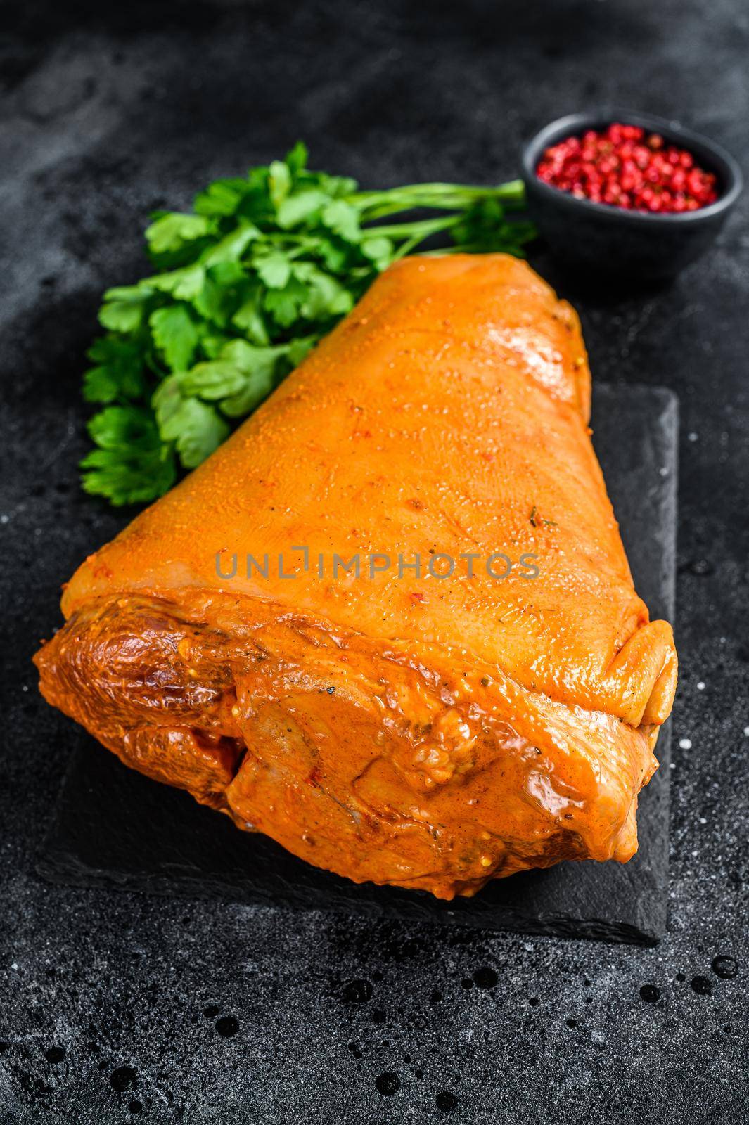 Raw pork leg with herbs and marinate on table. Black background. Top view by Composter