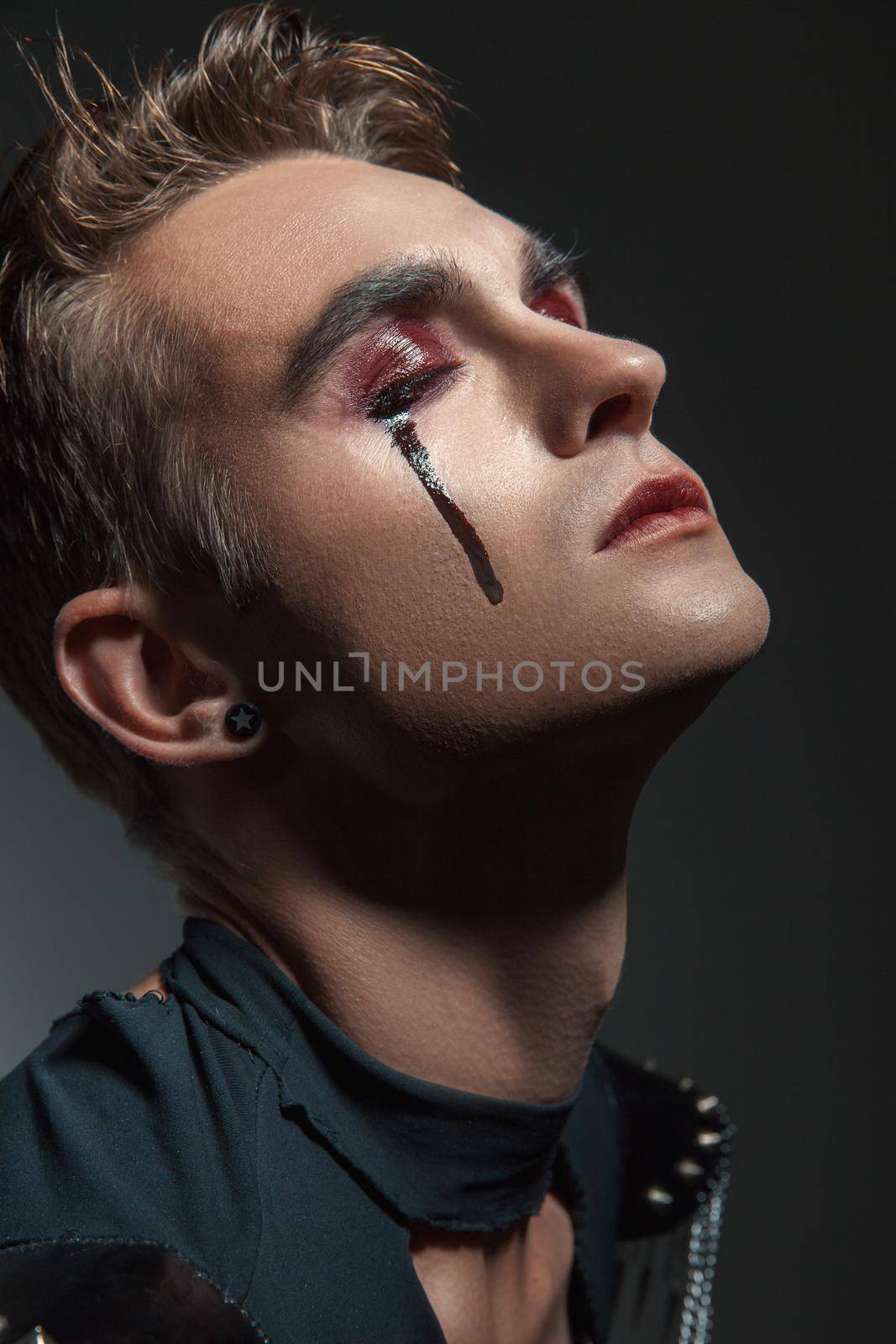 a young man with make up and painted tears. his eyes closed. Isolated.