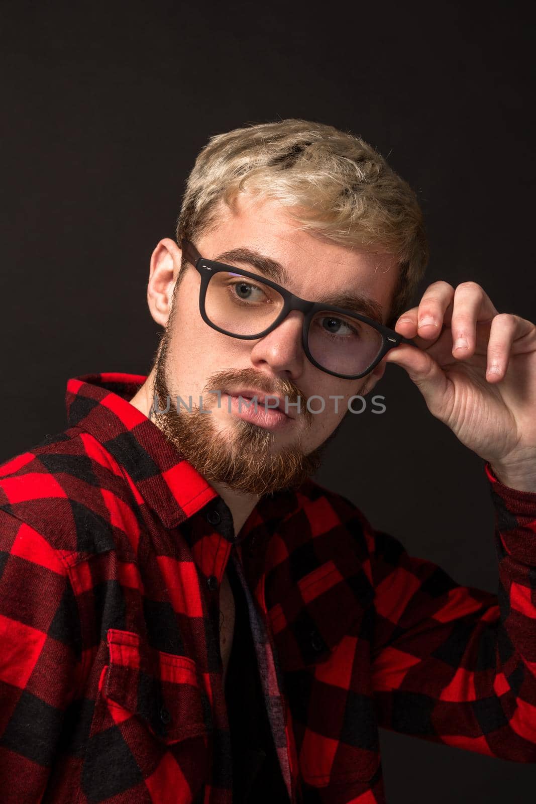 Close-up portrait of attractive young bearded hipster man wearing glasses dressed in shirt in a cage isolated over black background. Studio shot