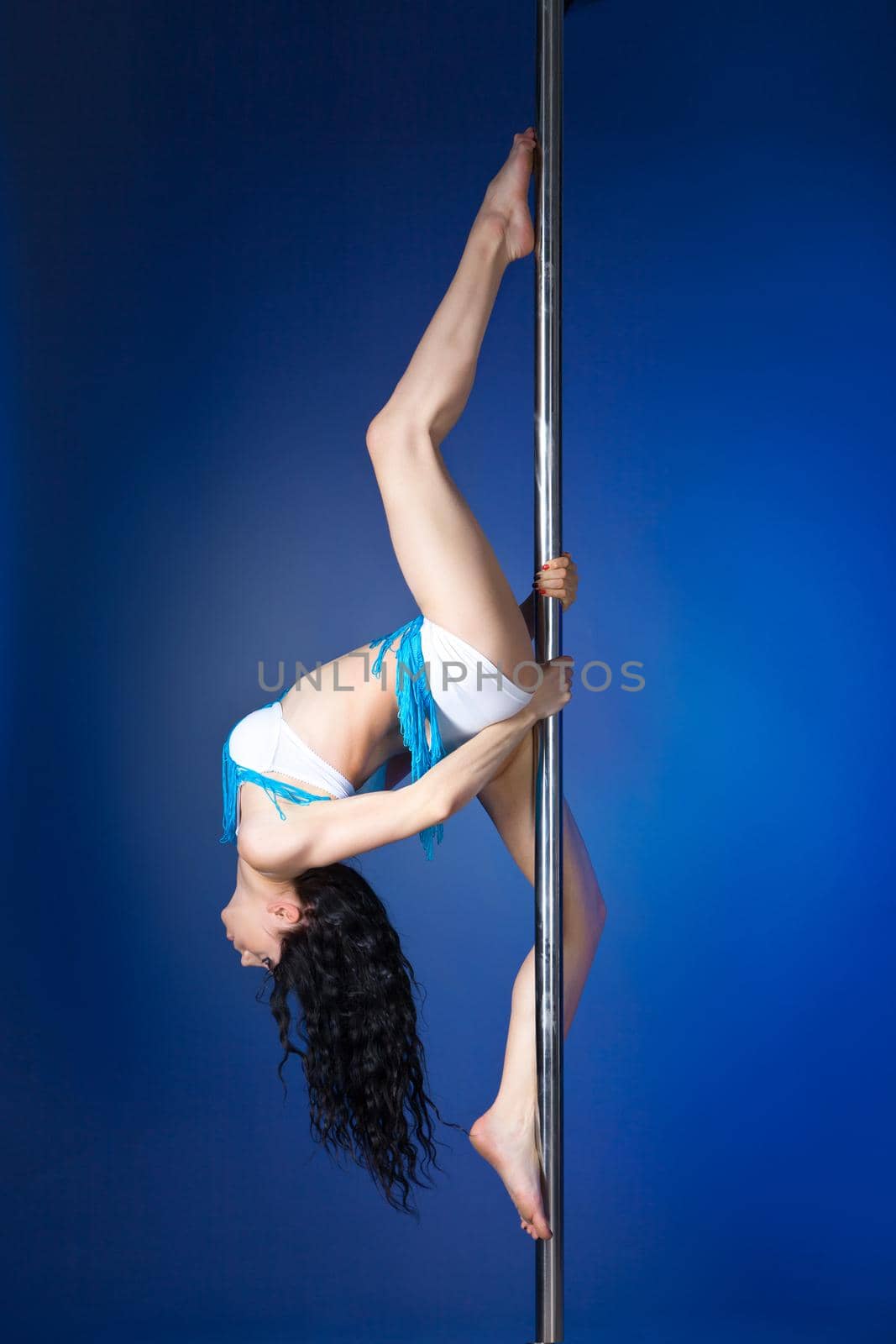 Young slim pole dance woman doing exercise against blue background