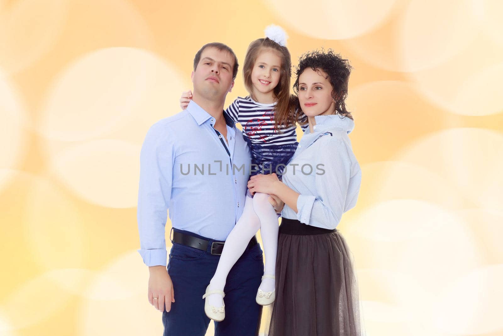 Happy young family, mom dad and little daughter.Parents keep the girl in her arms , and she hugs their neck.Brown festive, Christmas background with white snowflakes, circles.