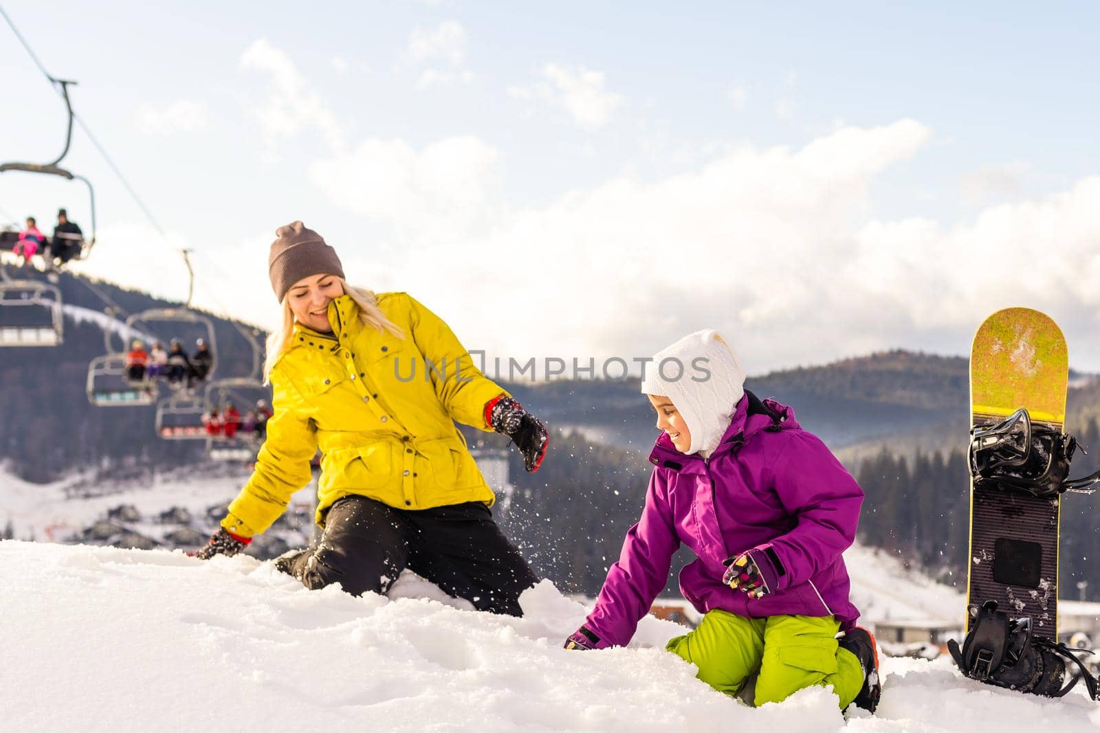 Mother and daughter with snowboards are playing in the snow