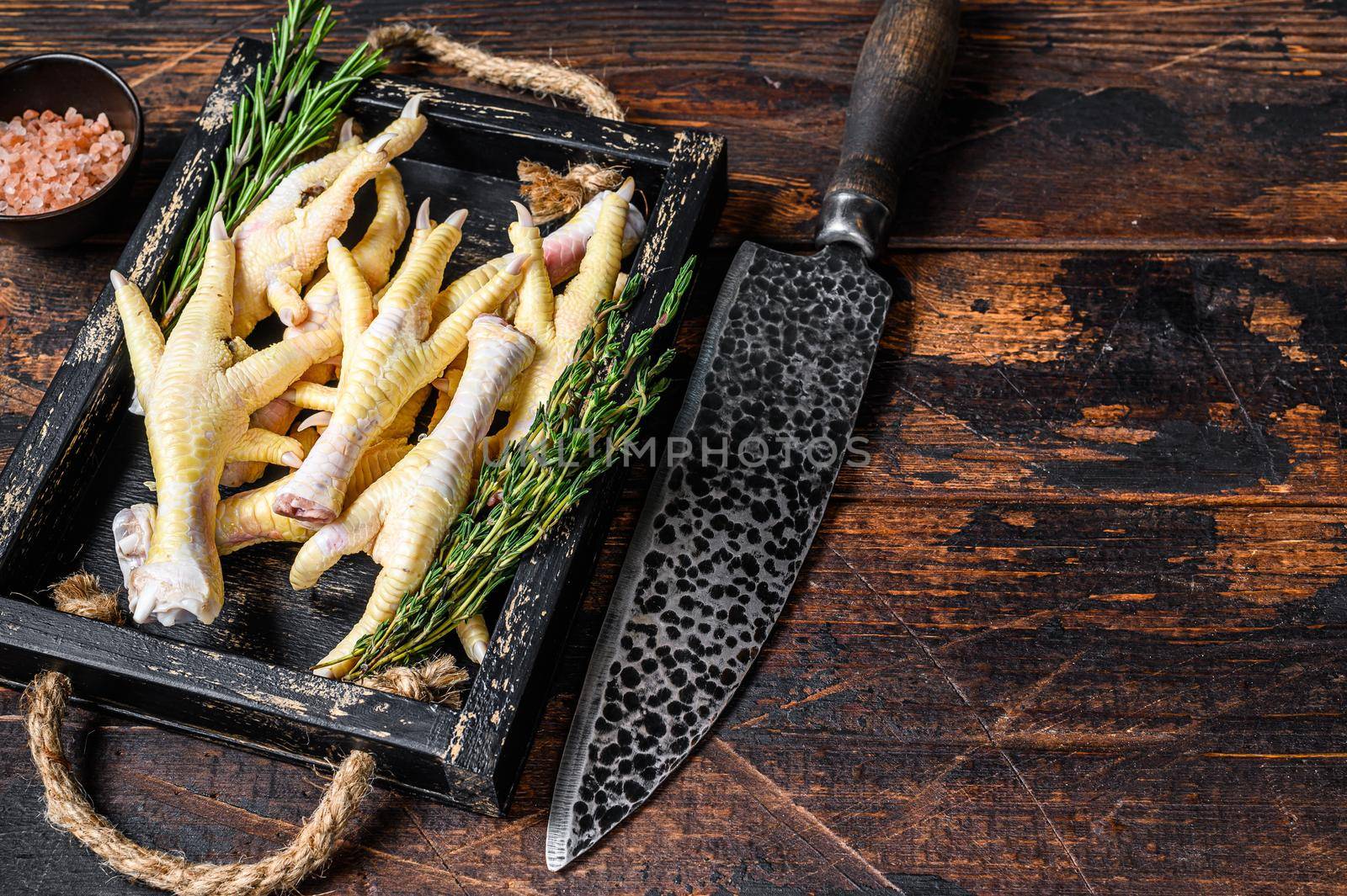 Raw Chicken paws feets on butcher chopping board with knife. Dark wooden background. Top view. Copy space.
