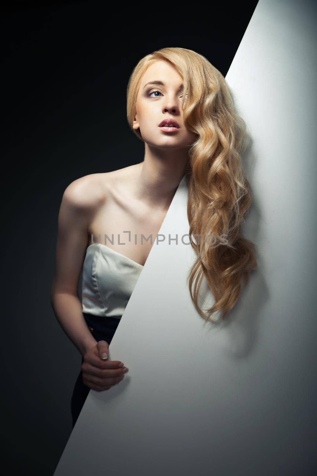 pretty blond model hiding behind a big blank sheet of paper and looking aside.
