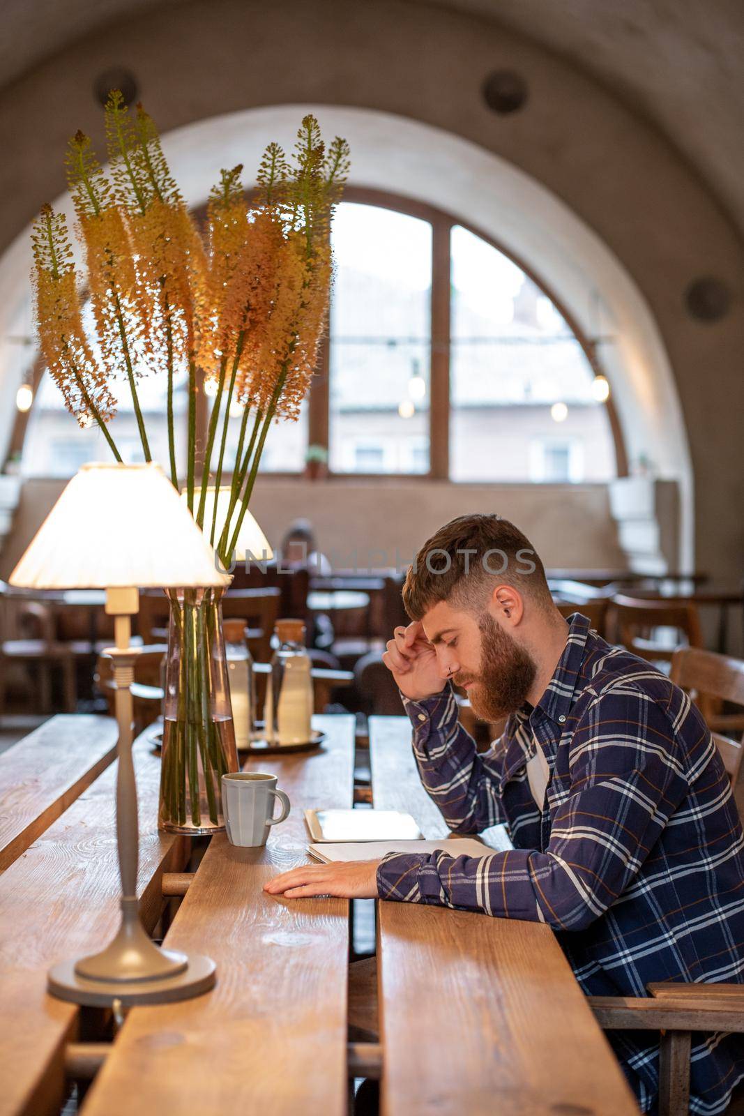 Young bearded businessman sits in cafe, home at table and writes in notebook, near lies tablet computer. Man is working, studying. Online education, marketing, training.